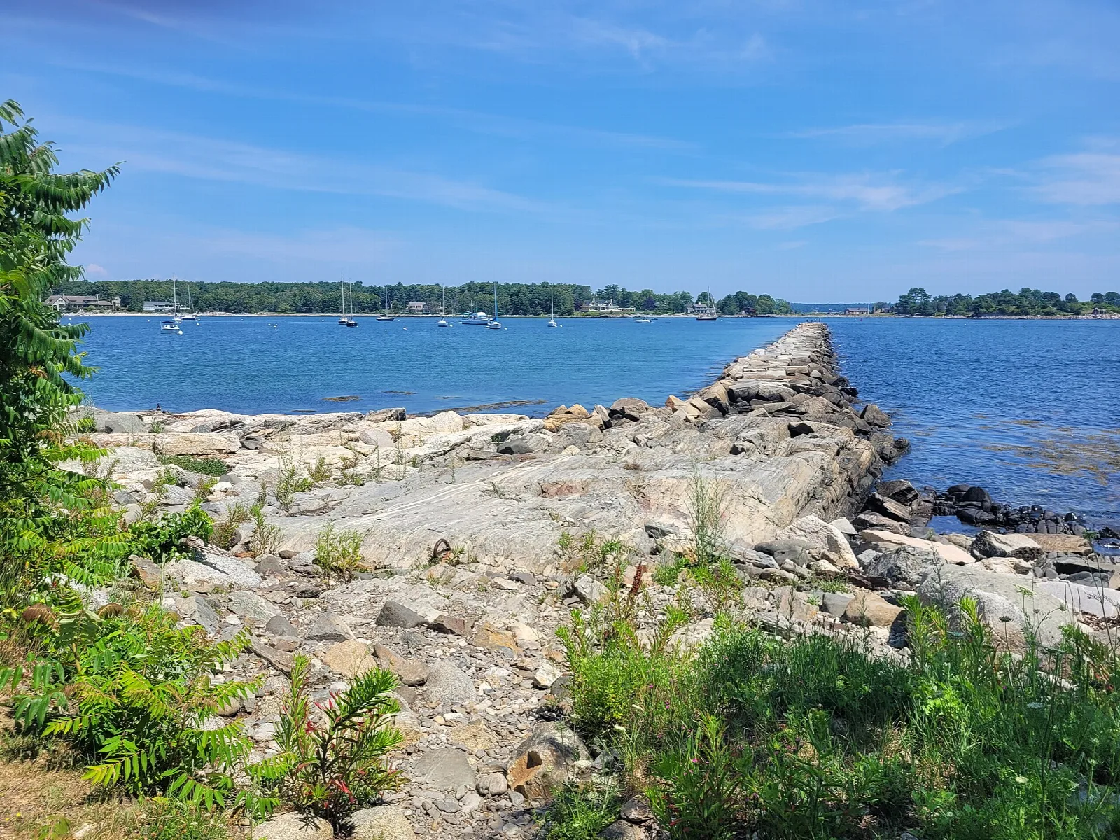 Rocky breakwater extending into blue water under a partly cloudy sky