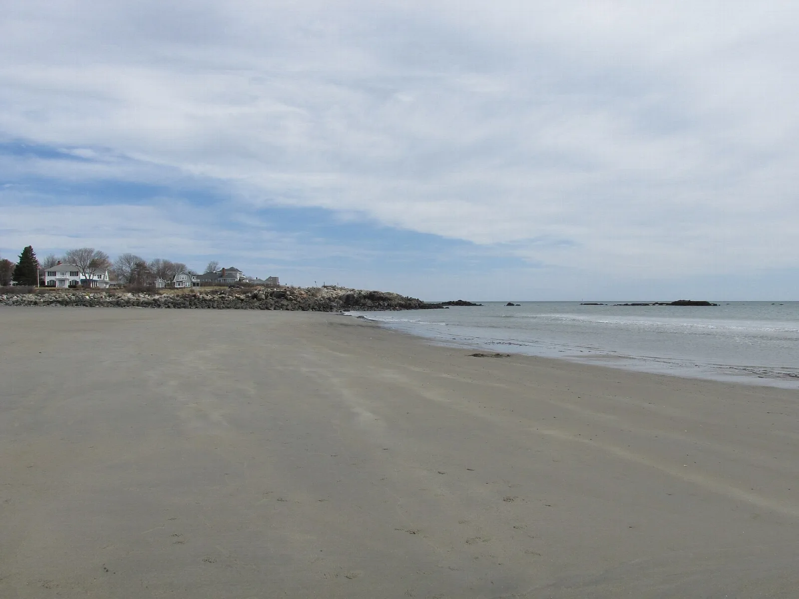 Wide empty sand beach at low tide with houses on a distant point