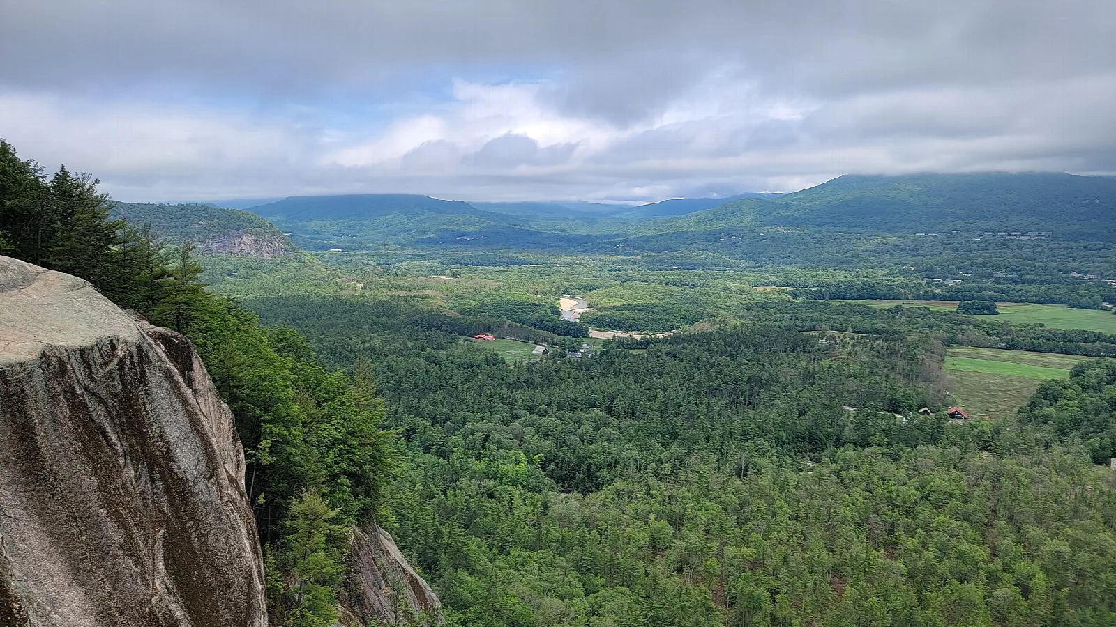 View from a granite ledge over a forested valley toward distant mountains