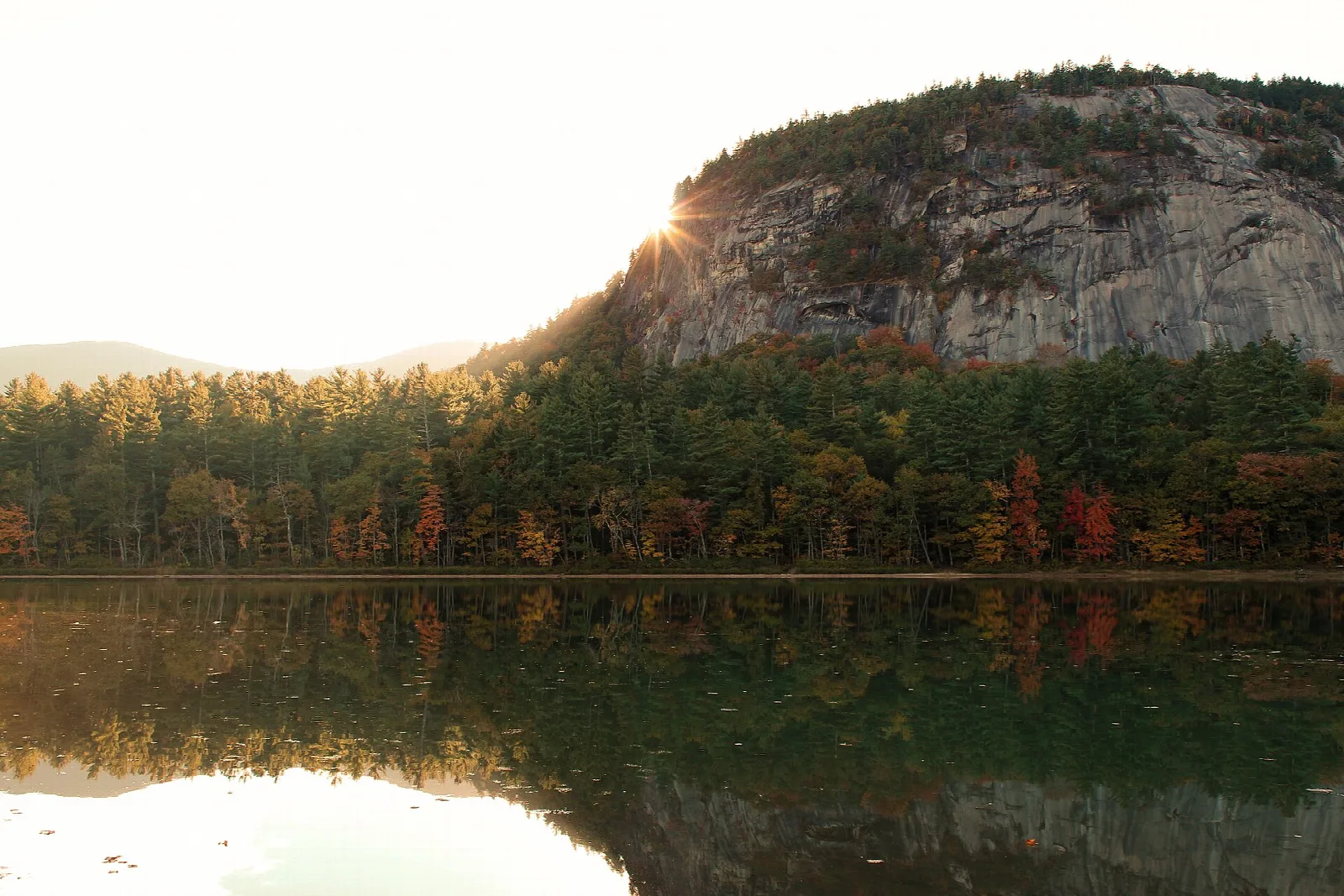 Granite ledge catching sunrise above autumn trees and still lake water