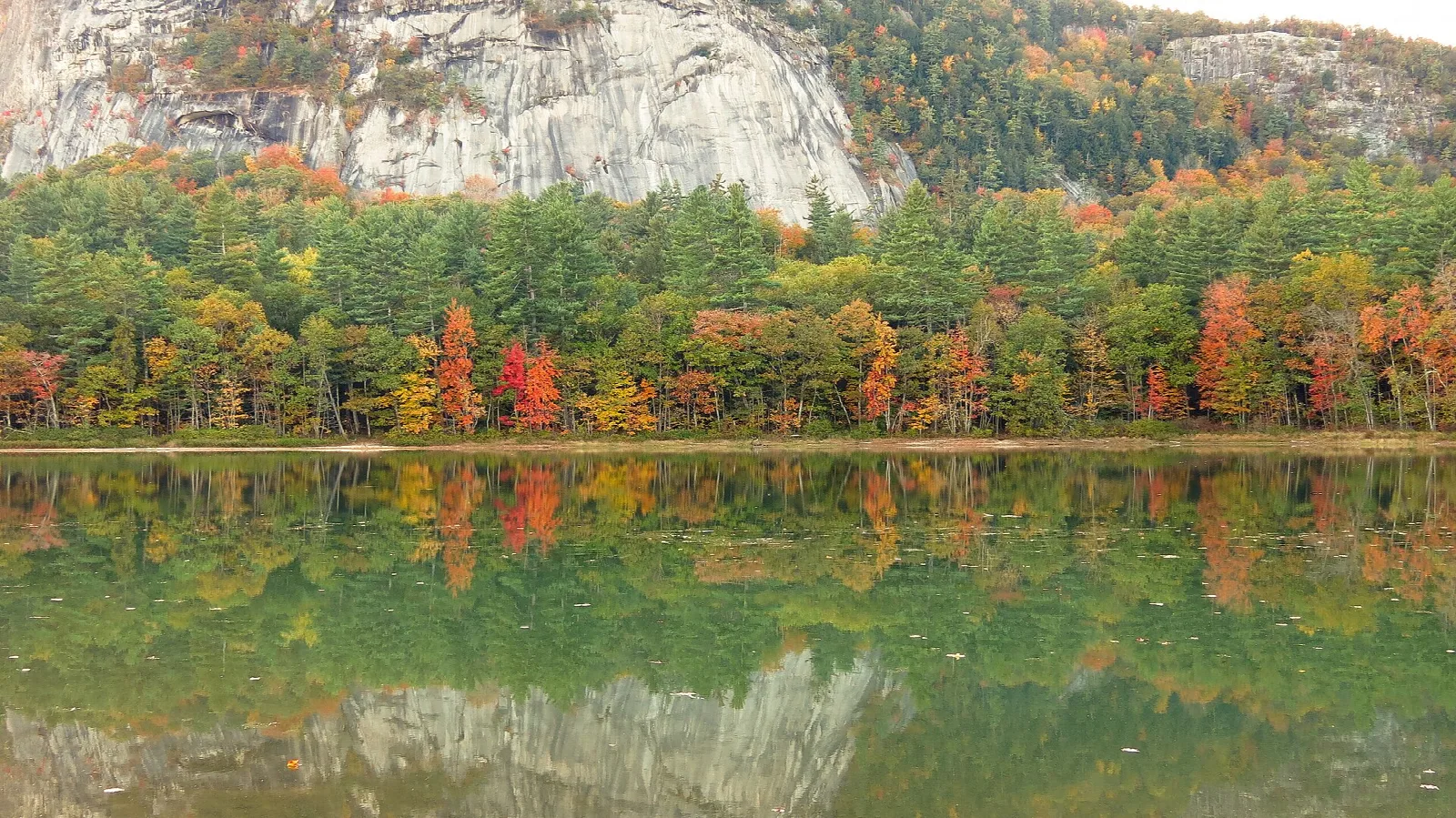 Autumn trees and a cliff face reflected in calm lake water