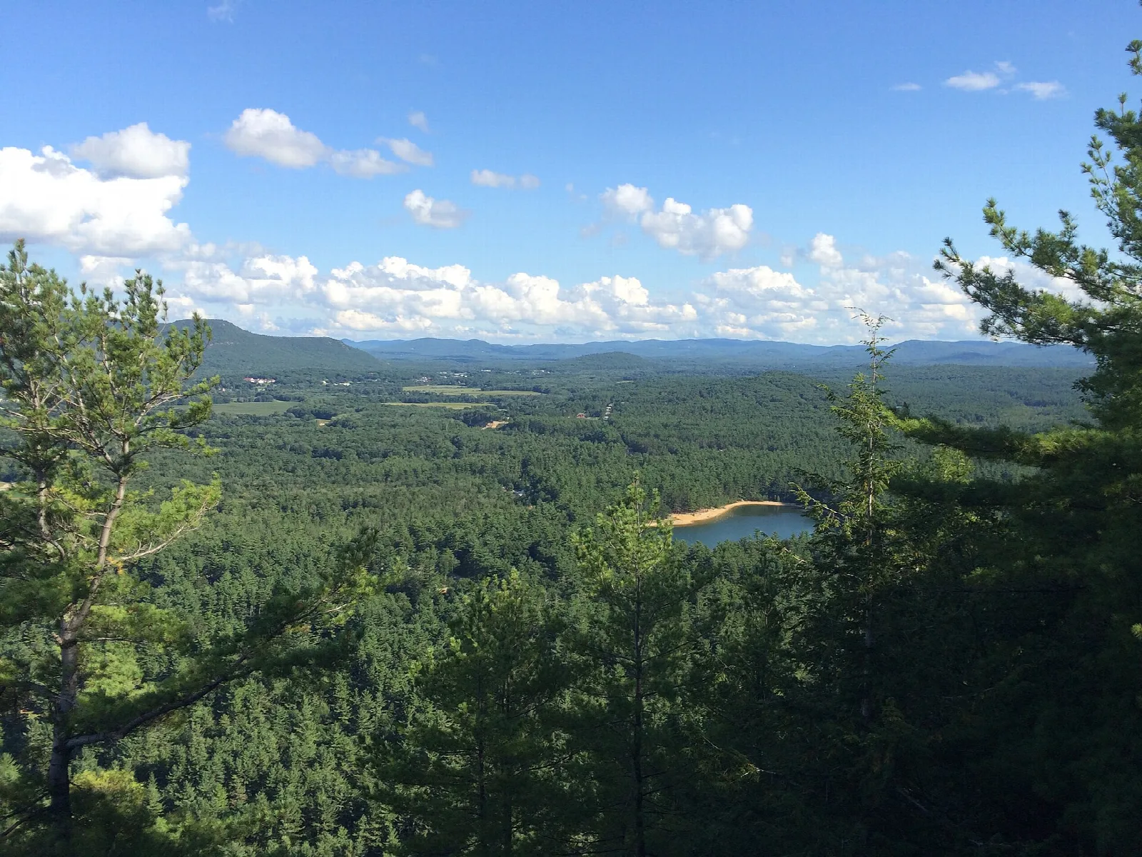 Wide view from a ledge over forest and a small lake in the valley