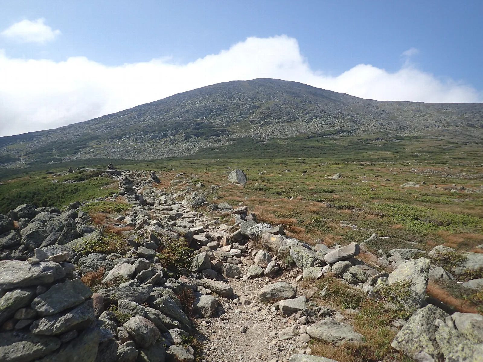 Rock-lined trail across a barren alpine slope toward a mountain peak