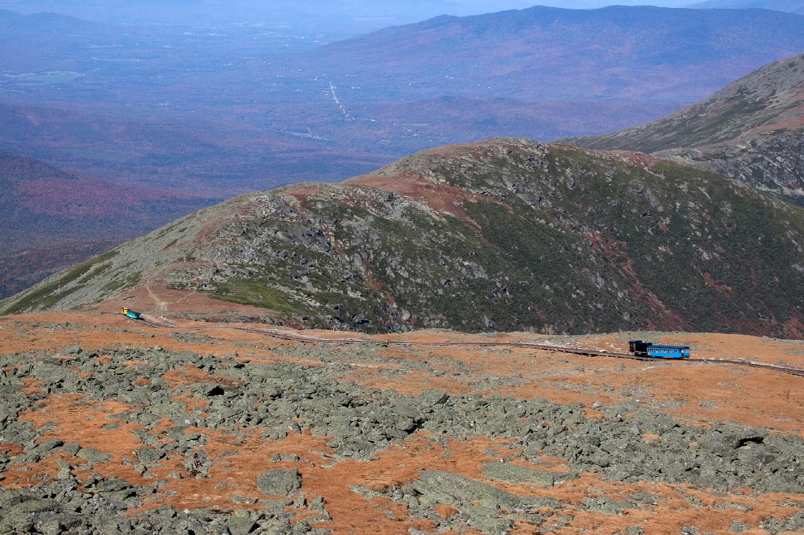 Rocky alpine ridge with orange tundra and a vehicle on the slope below