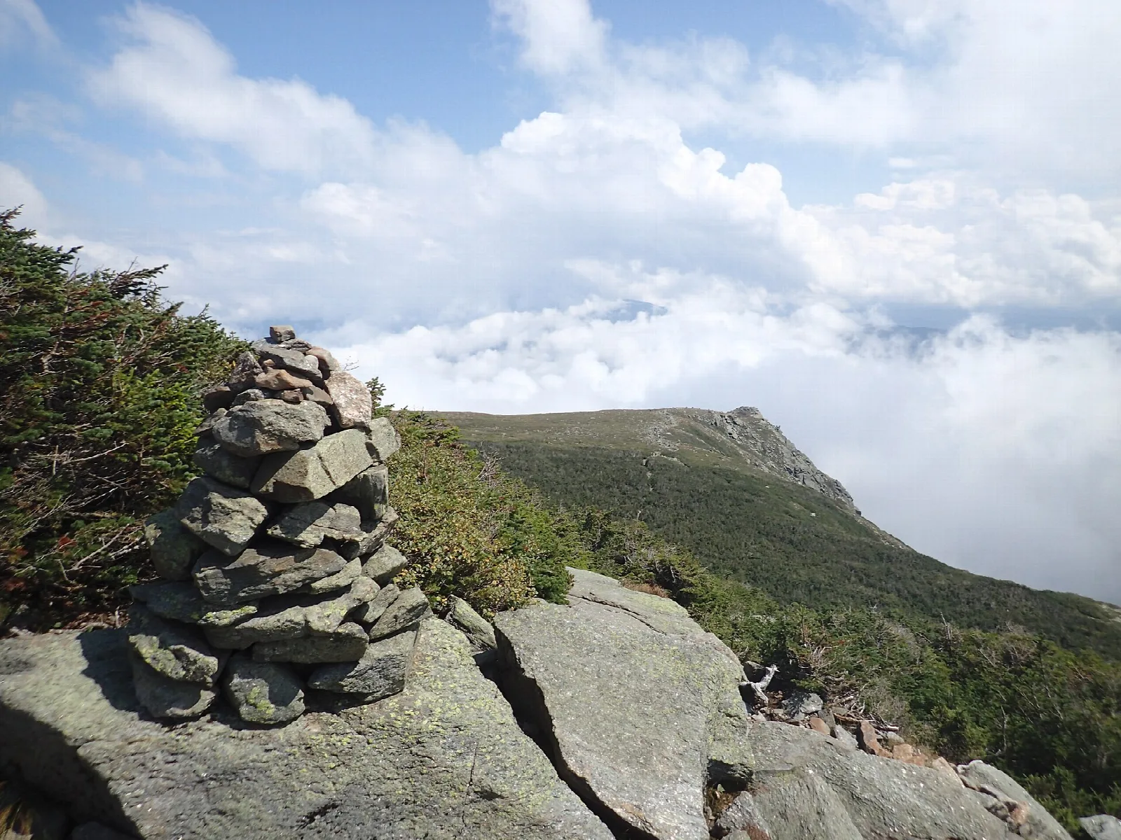 Stacked stone cairn on a rocky ledge above clouds