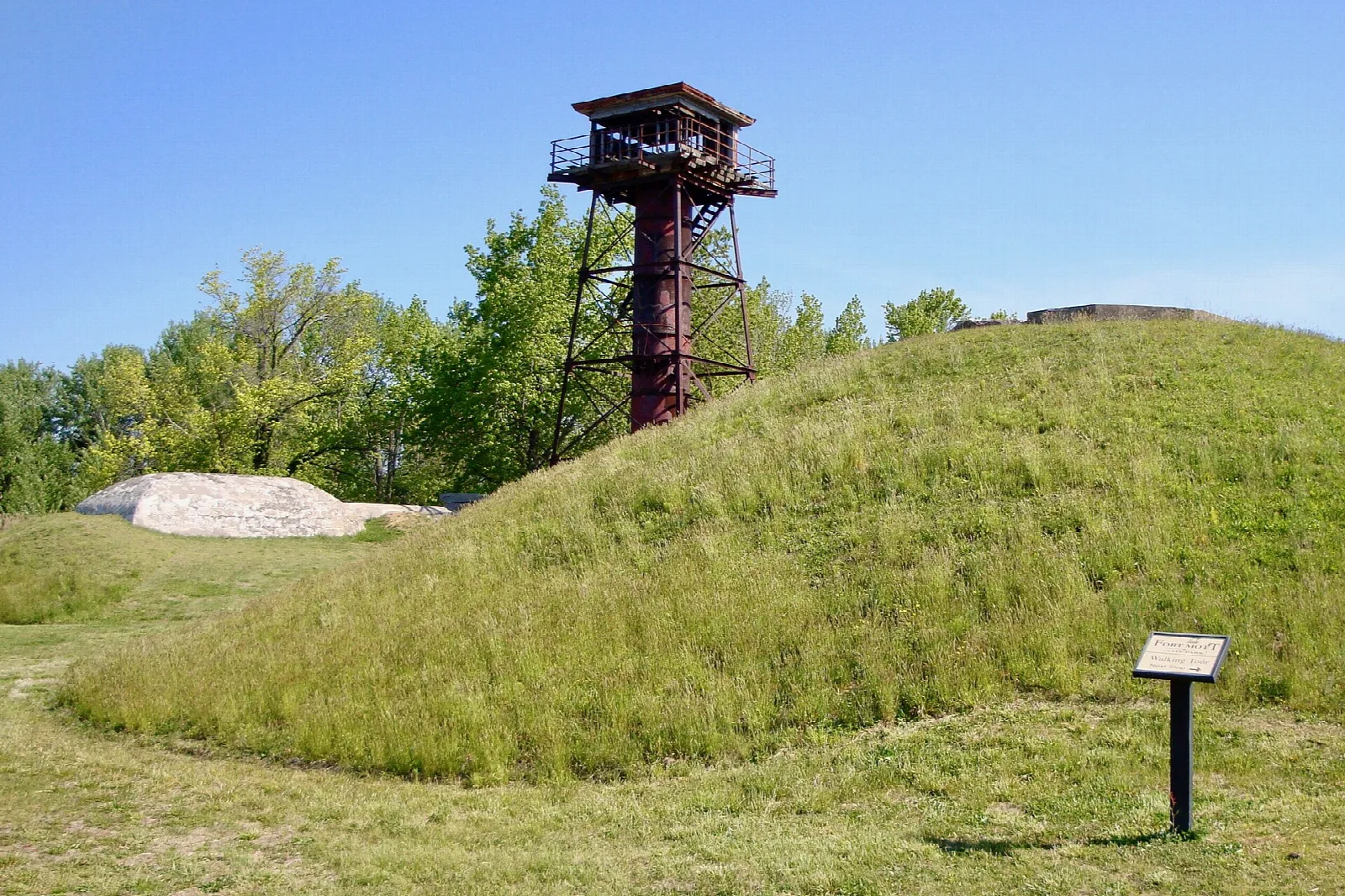 Red steel fire control tower behind a grassy earthen mound