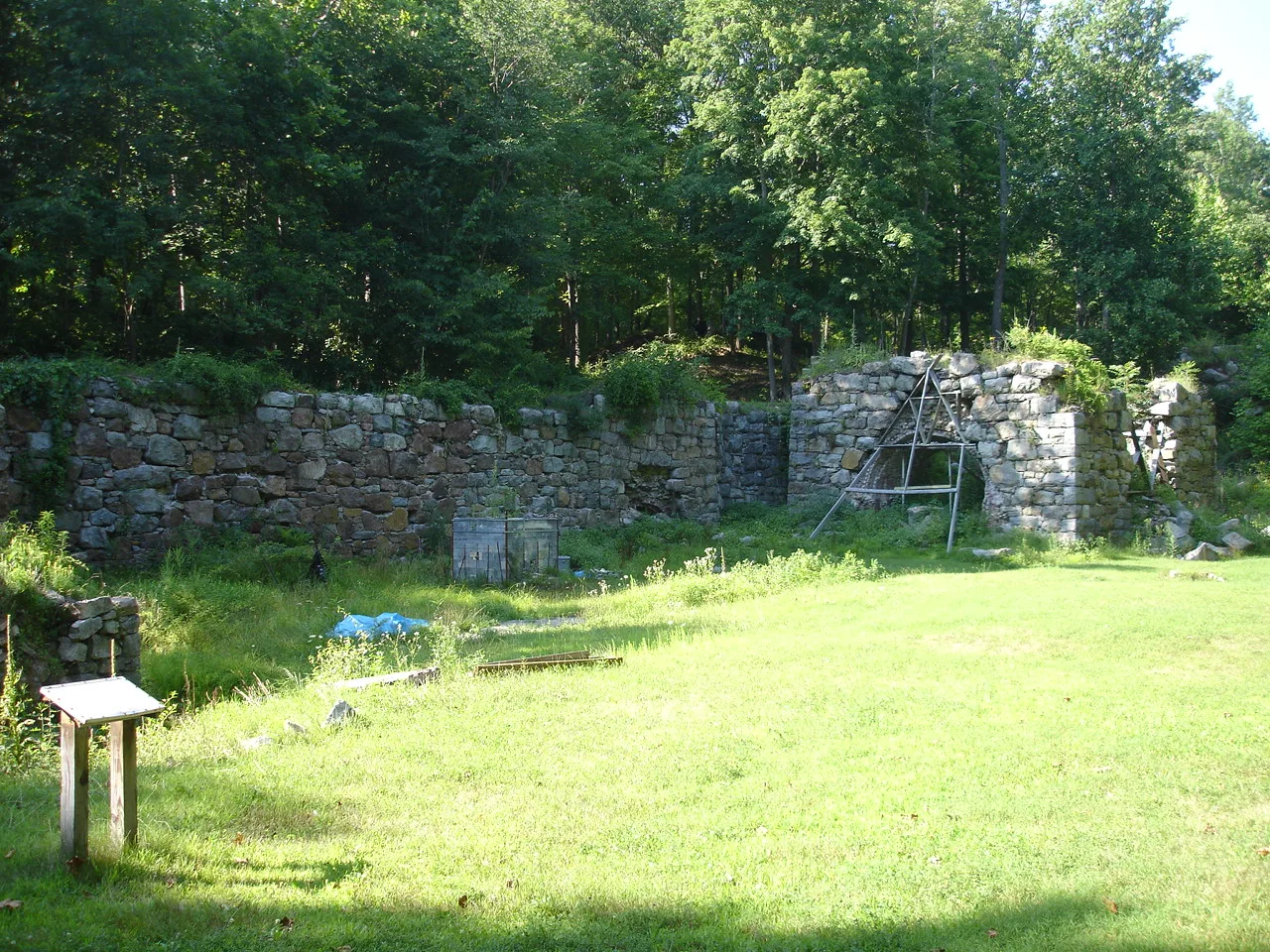 Low stone furnace wall at the edge of a mowed lawn in the woods