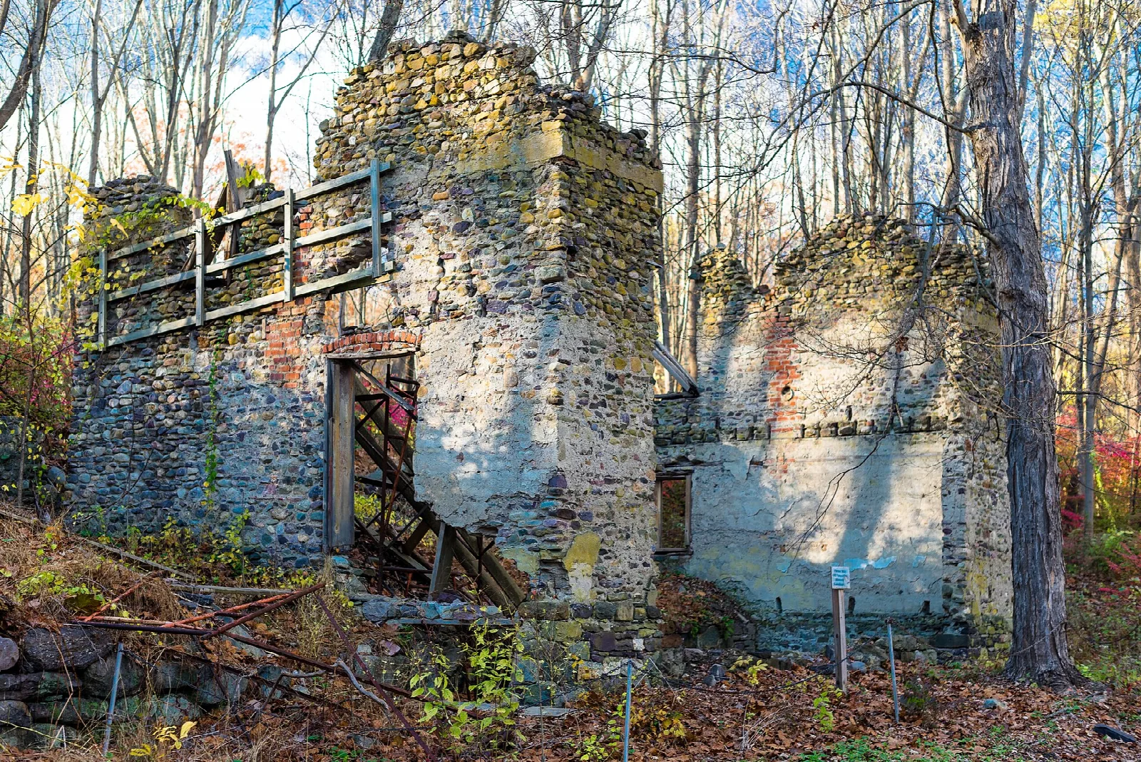 Ruined stone smelting building with wooden stairs among bare trees