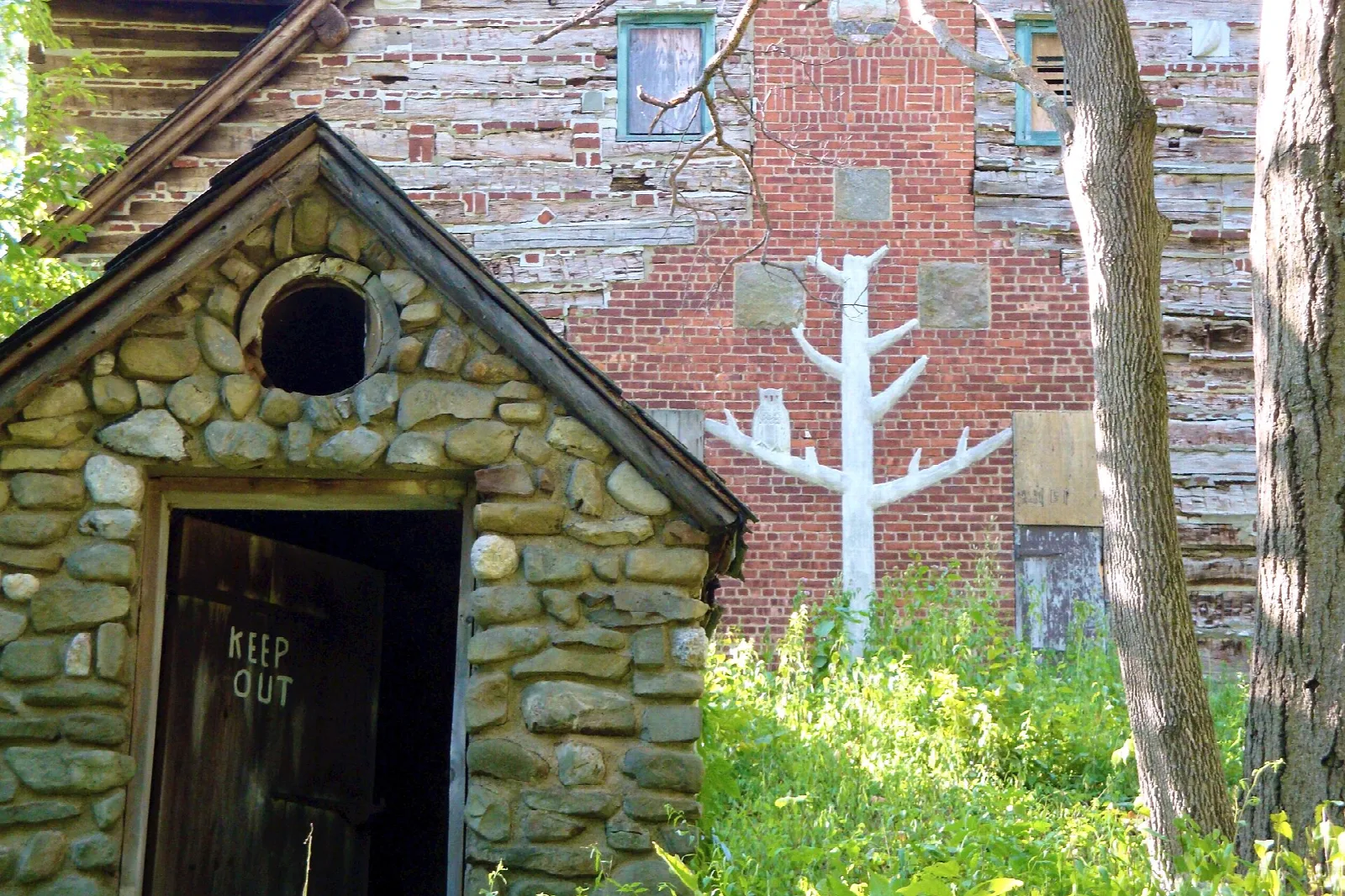 Small stone outbuilding in front of an old brick and wood farm building