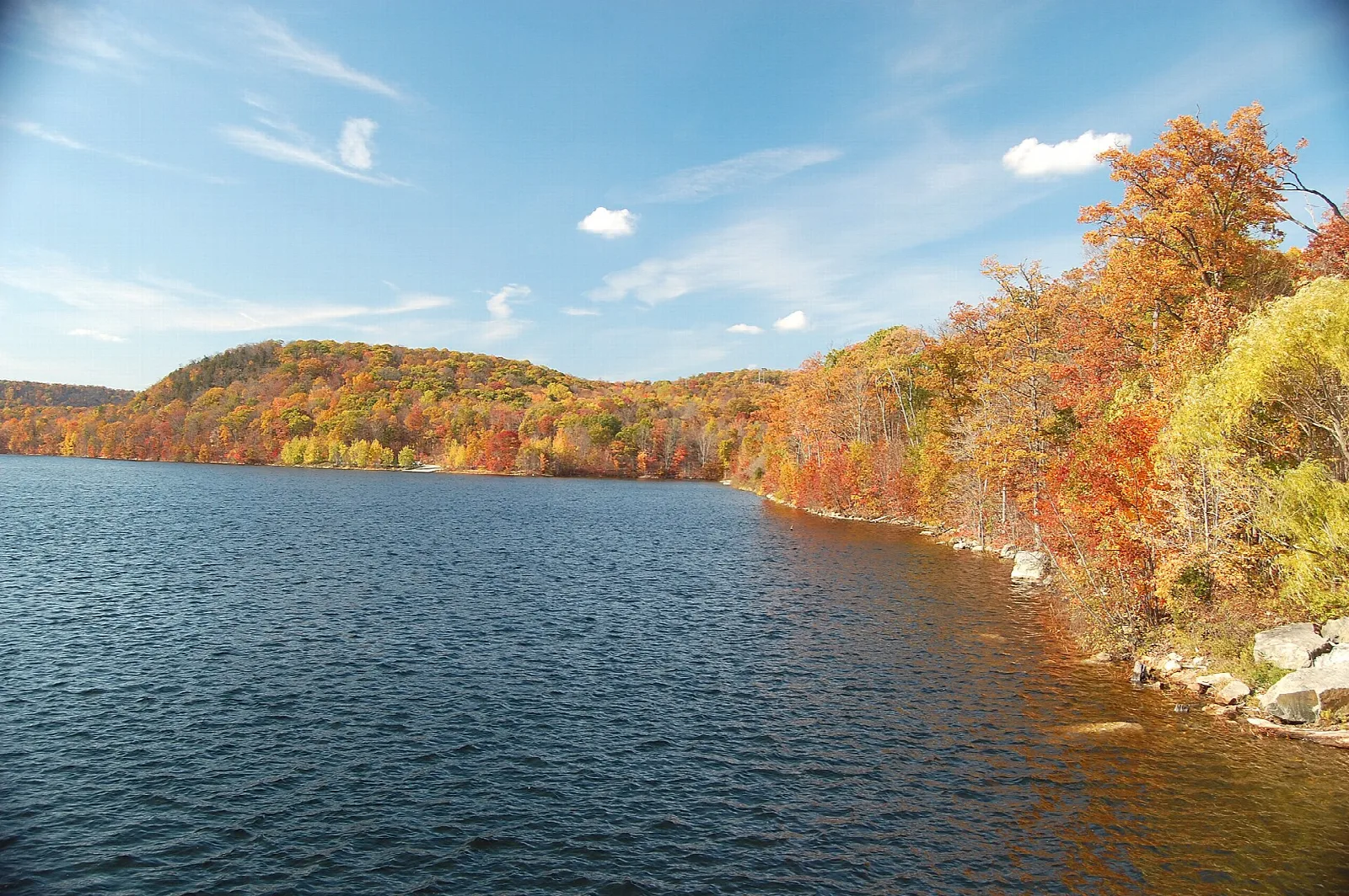Reservoir curving past a rocky shore with orange fall trees