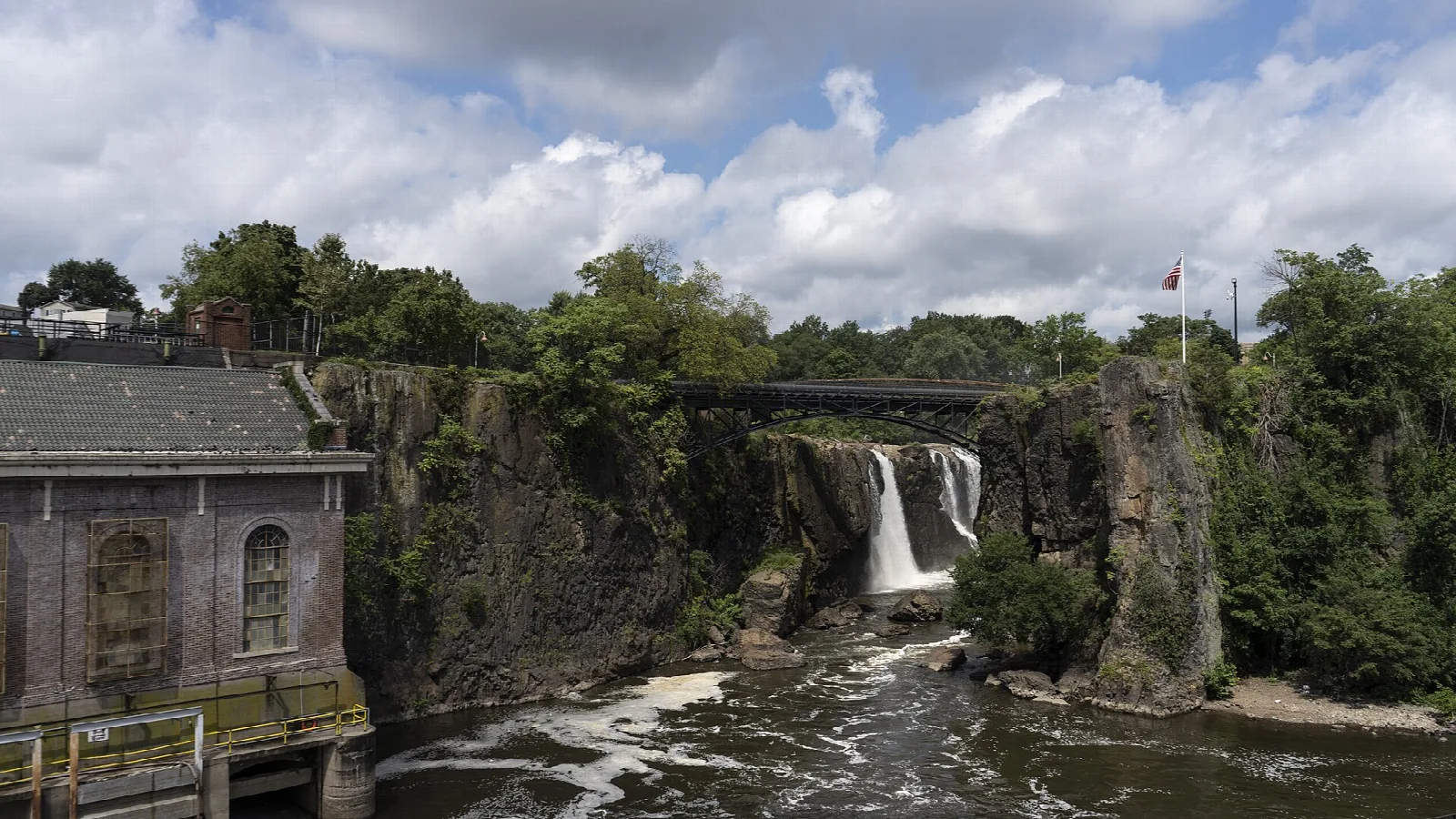 Waterfall dropping into a rocky gorge beside an old brick power house