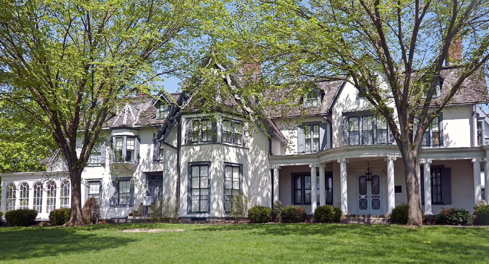 White manor house with a porch seen across a green lawn