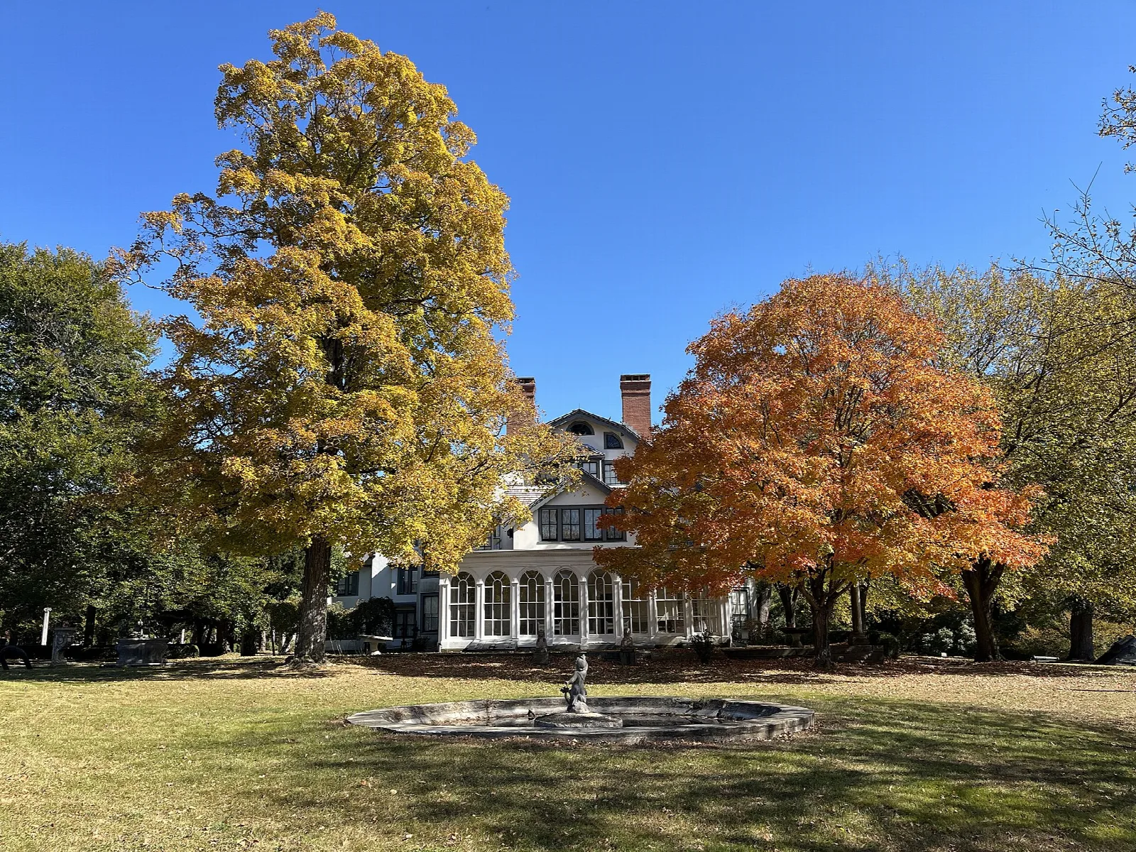 Manor house behind autumn trees and a lawn with a fountain