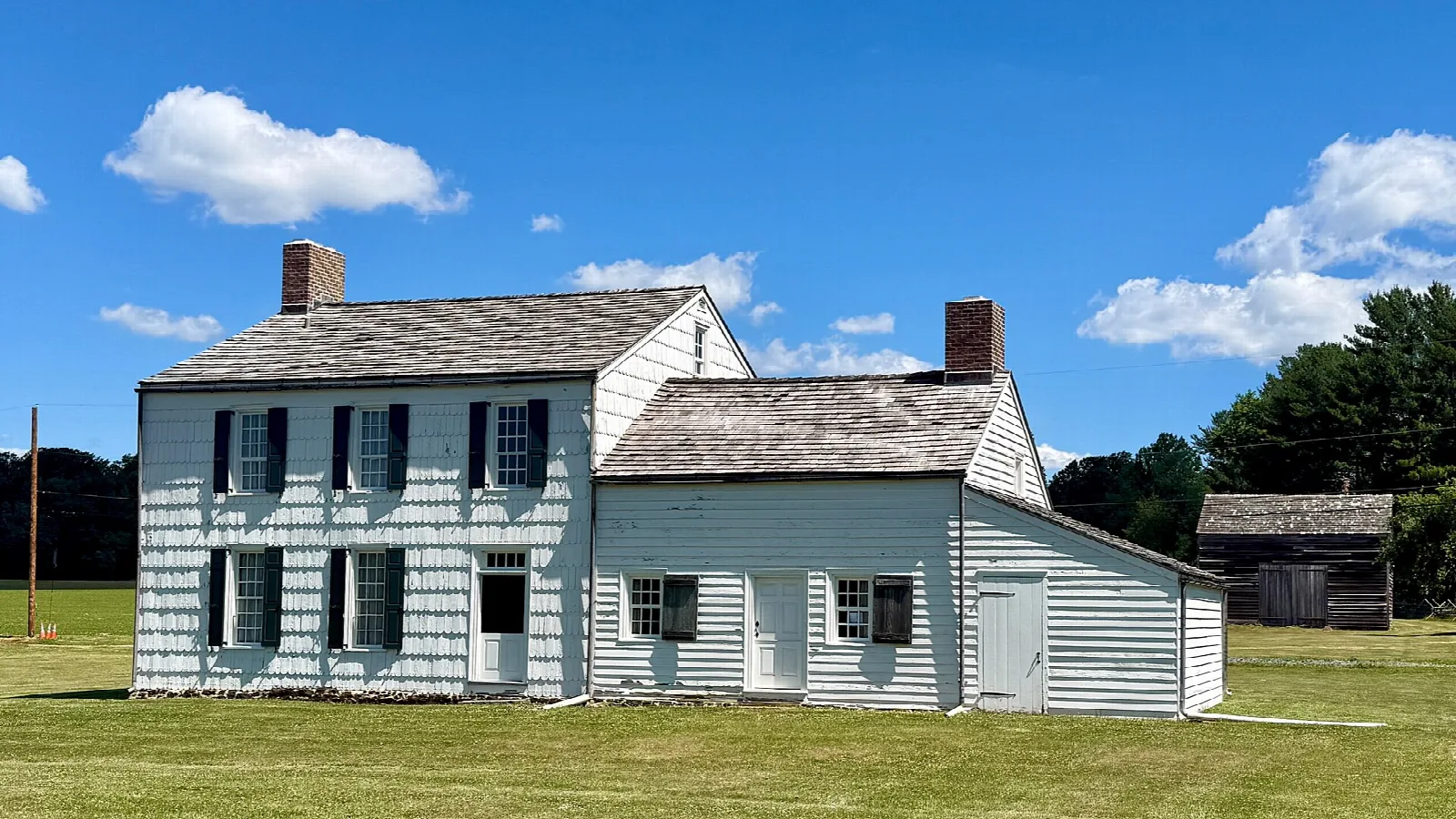 White farmhouse with chimneys and a barn on a lawn