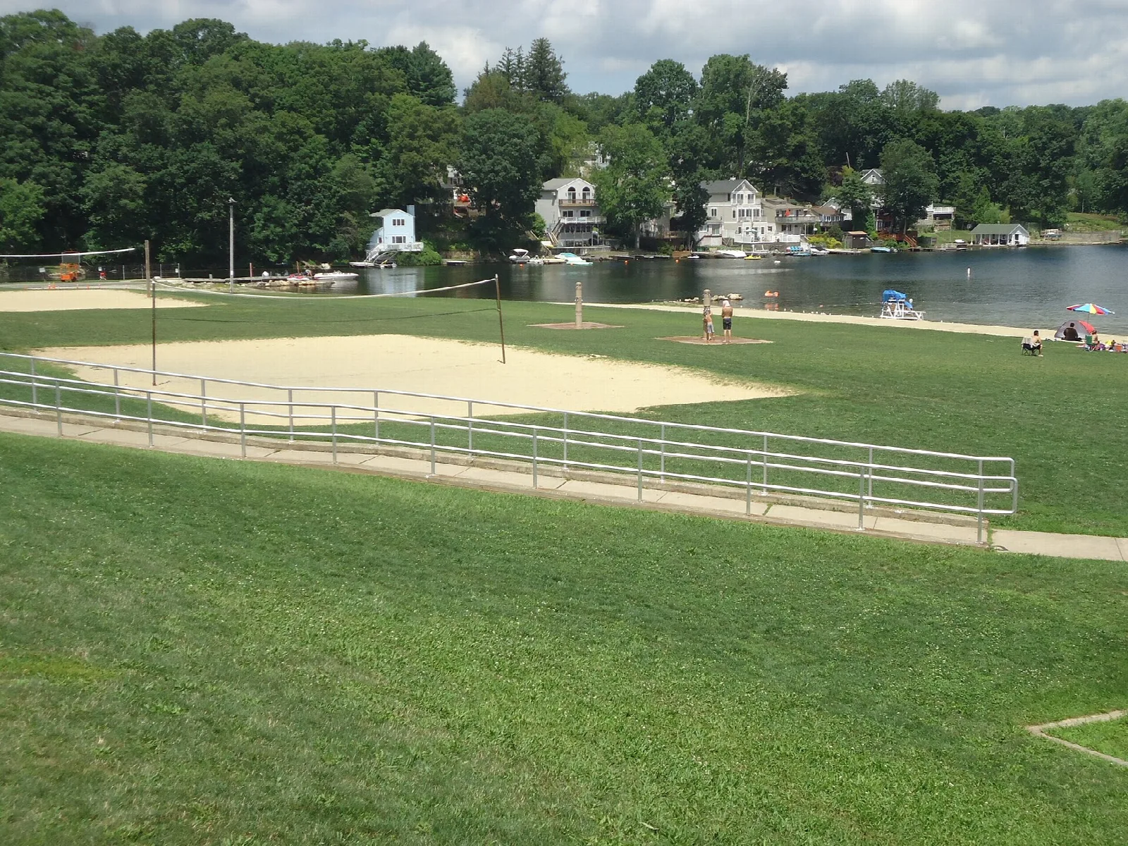 Lawn, sand volleyball court and lake with houses beyond
