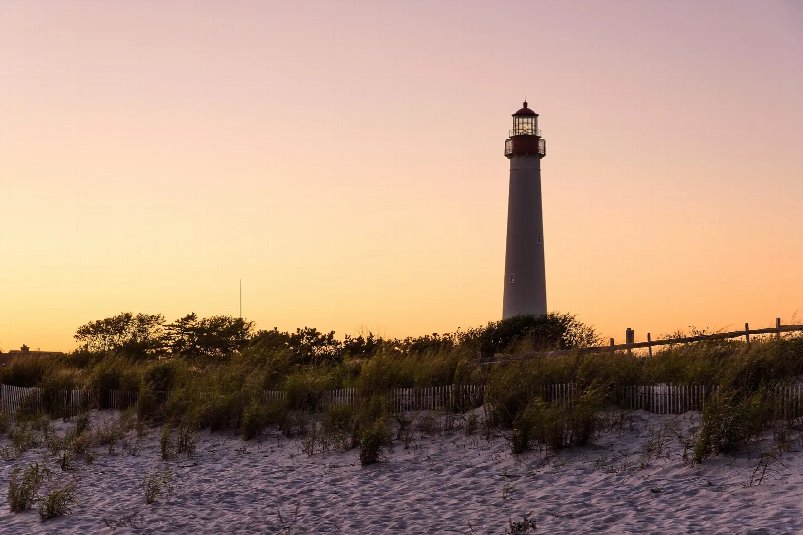 Lighthouse at sunset above dune grass and sand