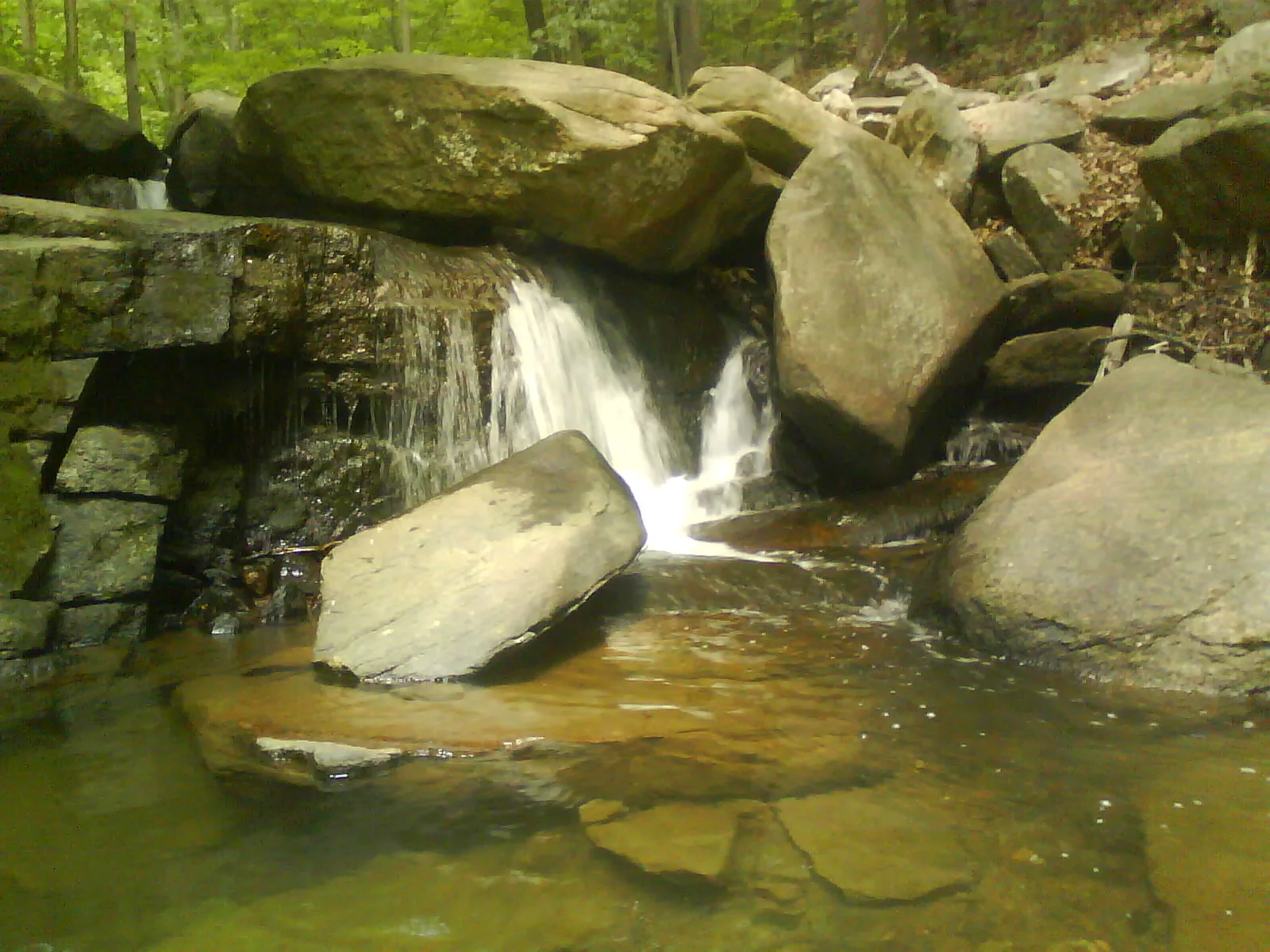 Small waterfall between mossy rocks and a stone wall