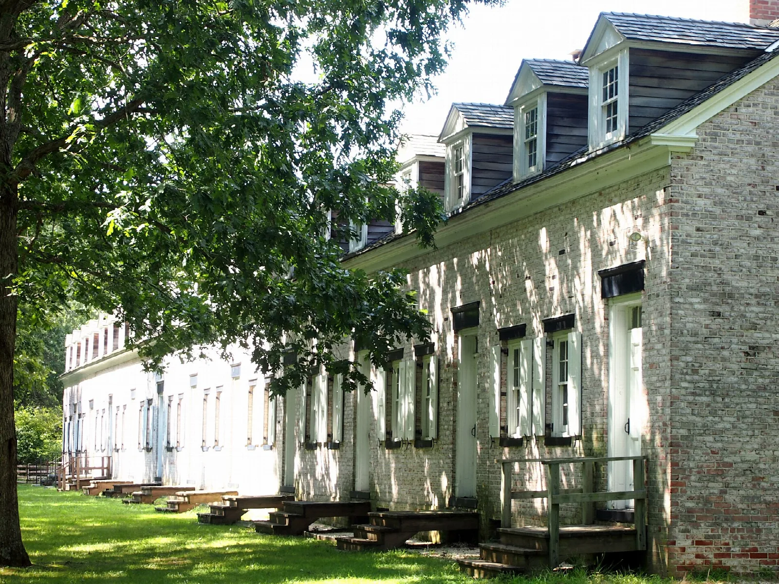 Long white row house with dormer windows beside a lawn
