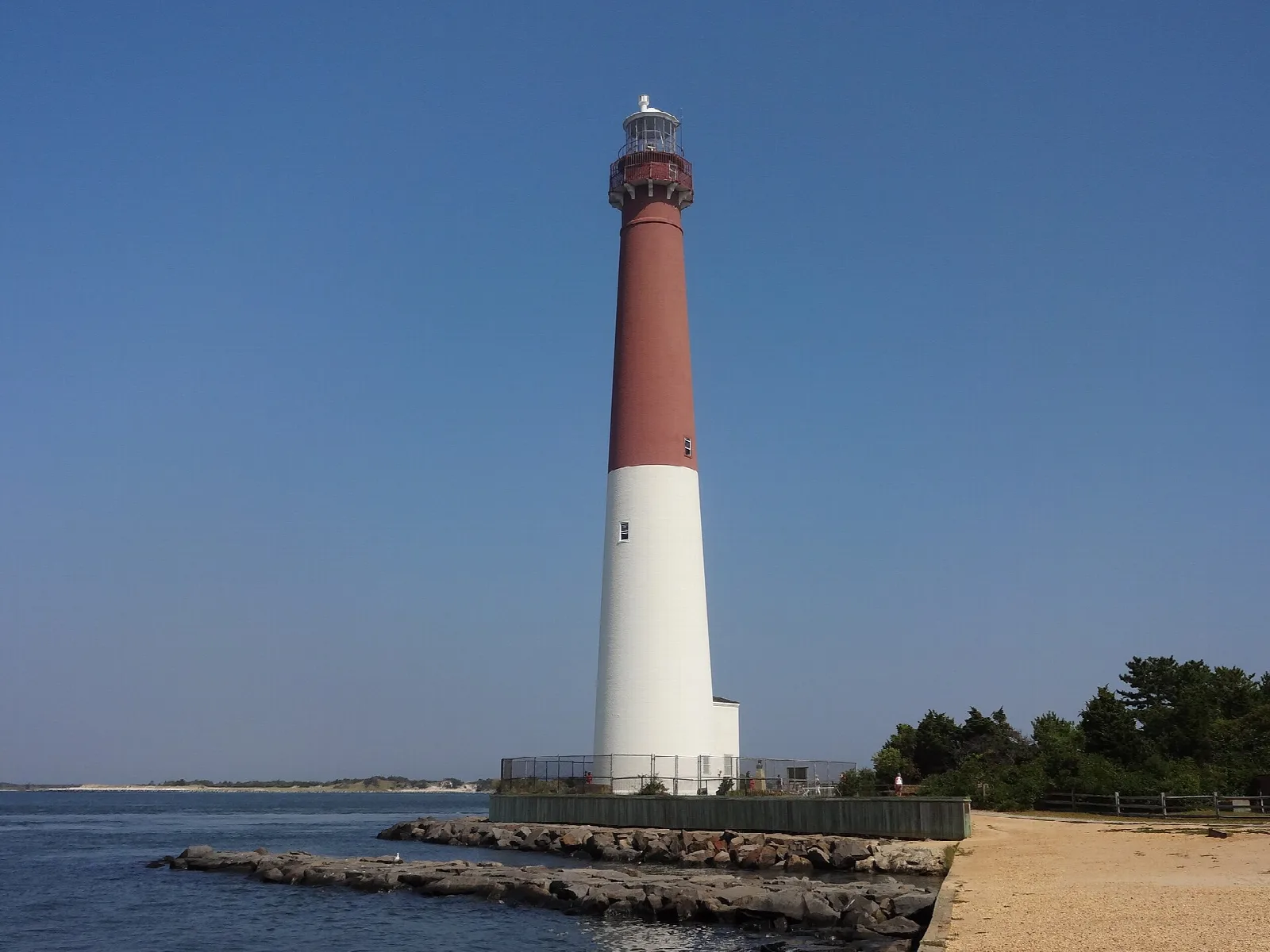 Lighthouse beside a rock jetty and sandy path on a clear day