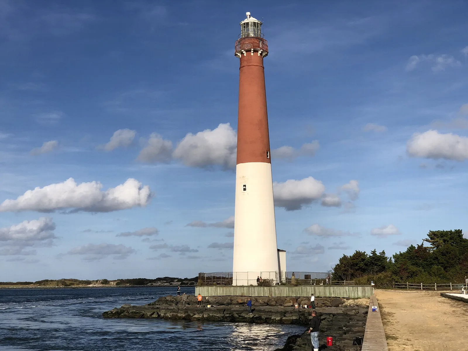 Red and white lighthouse beside the water under scattered clouds