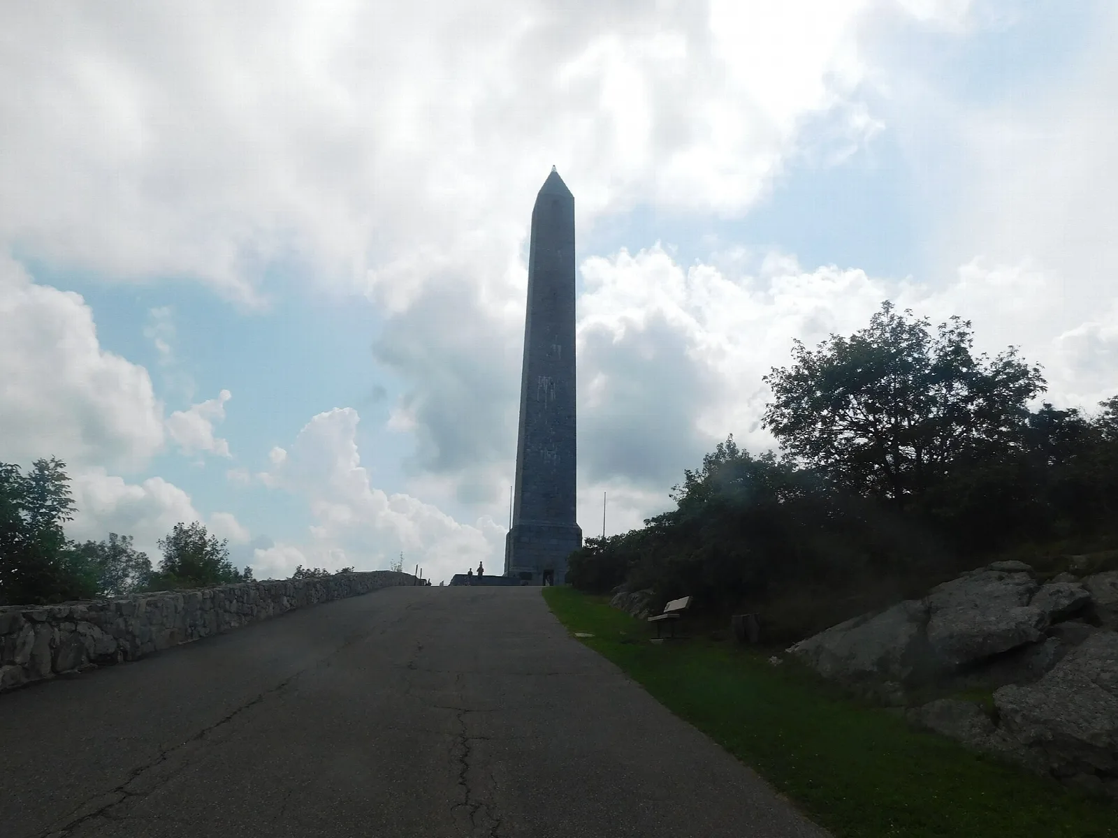 Stone obelisk at the end of a paved road beneath clouds