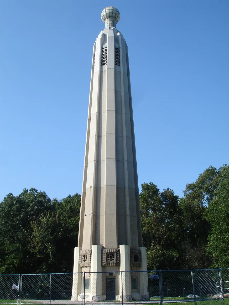 Tall pale concrete tower against a blue sky with trees behind