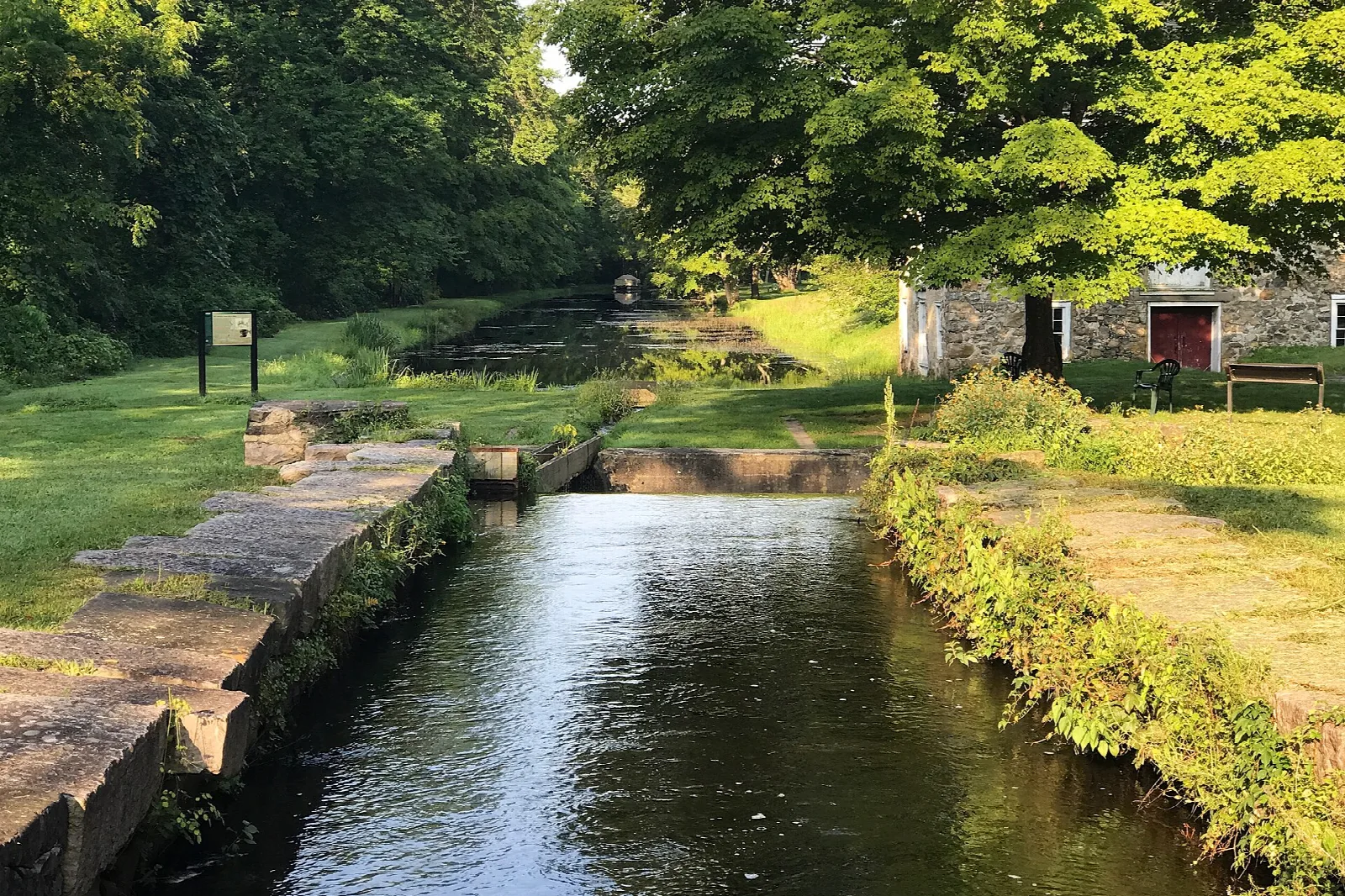 Stone-lined canal lock with grass banks and a building beyond