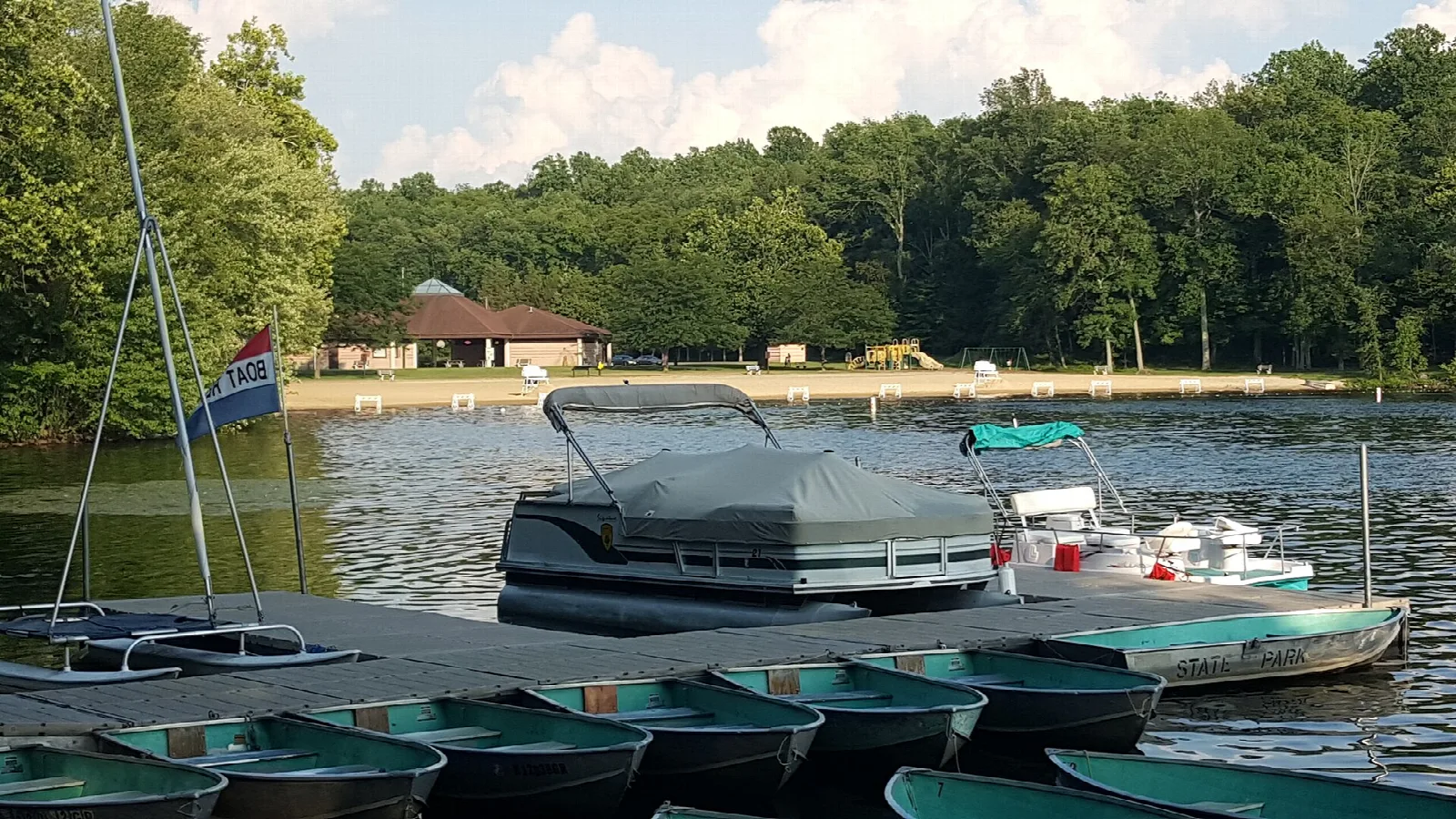 Rowboats and a pontoon boat tied at a dock on the lake
