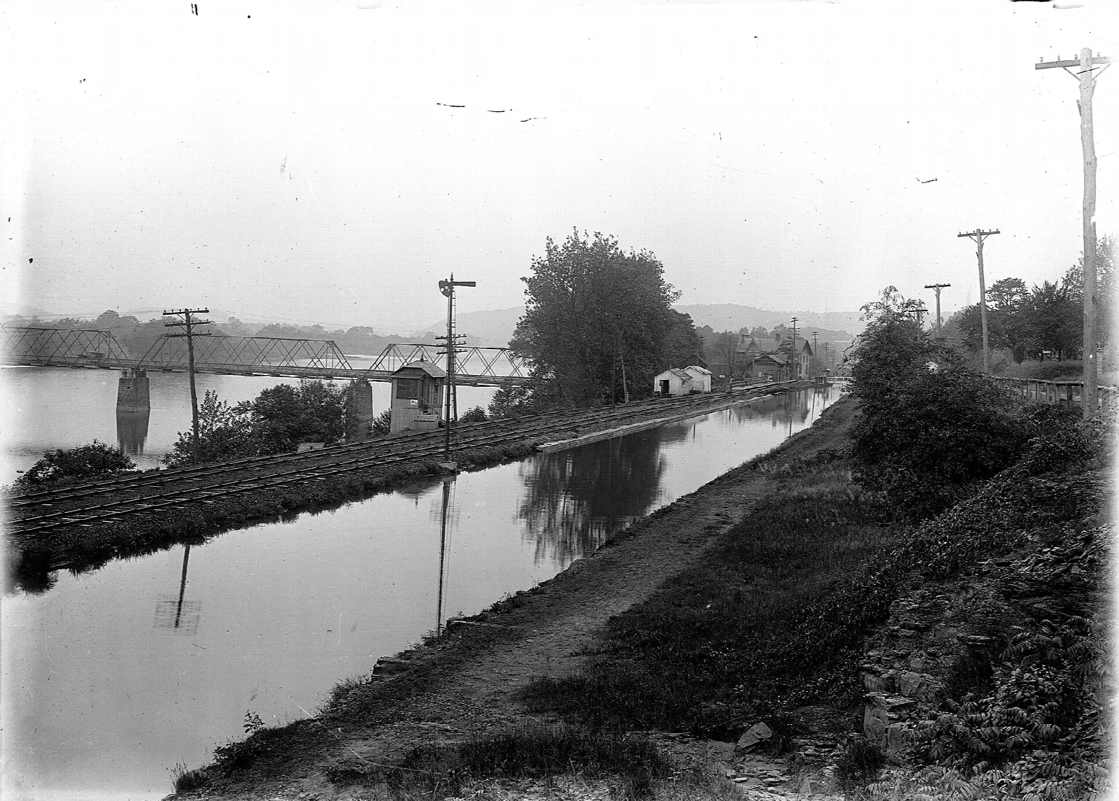 Black and white view of a canal with a rail line beside it