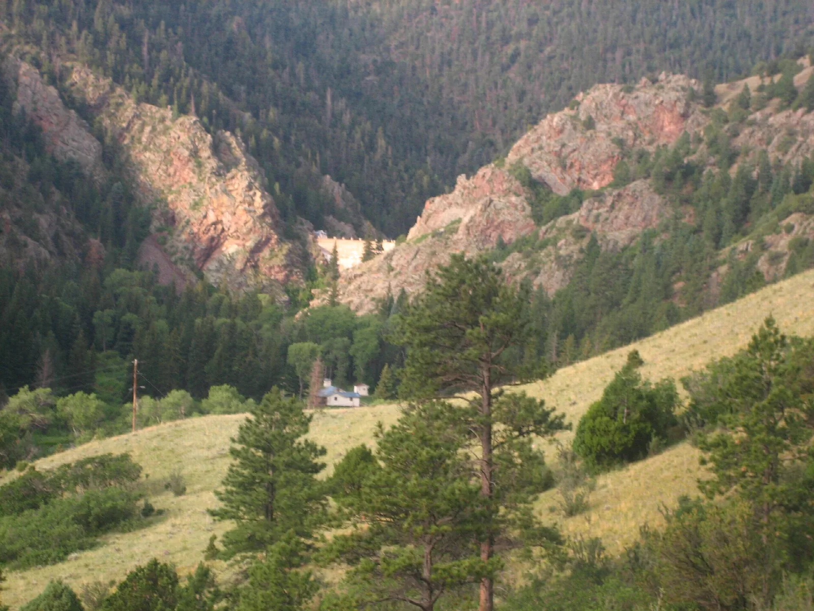 Mountain valley with red rock cliffs and forested slopes above a small building