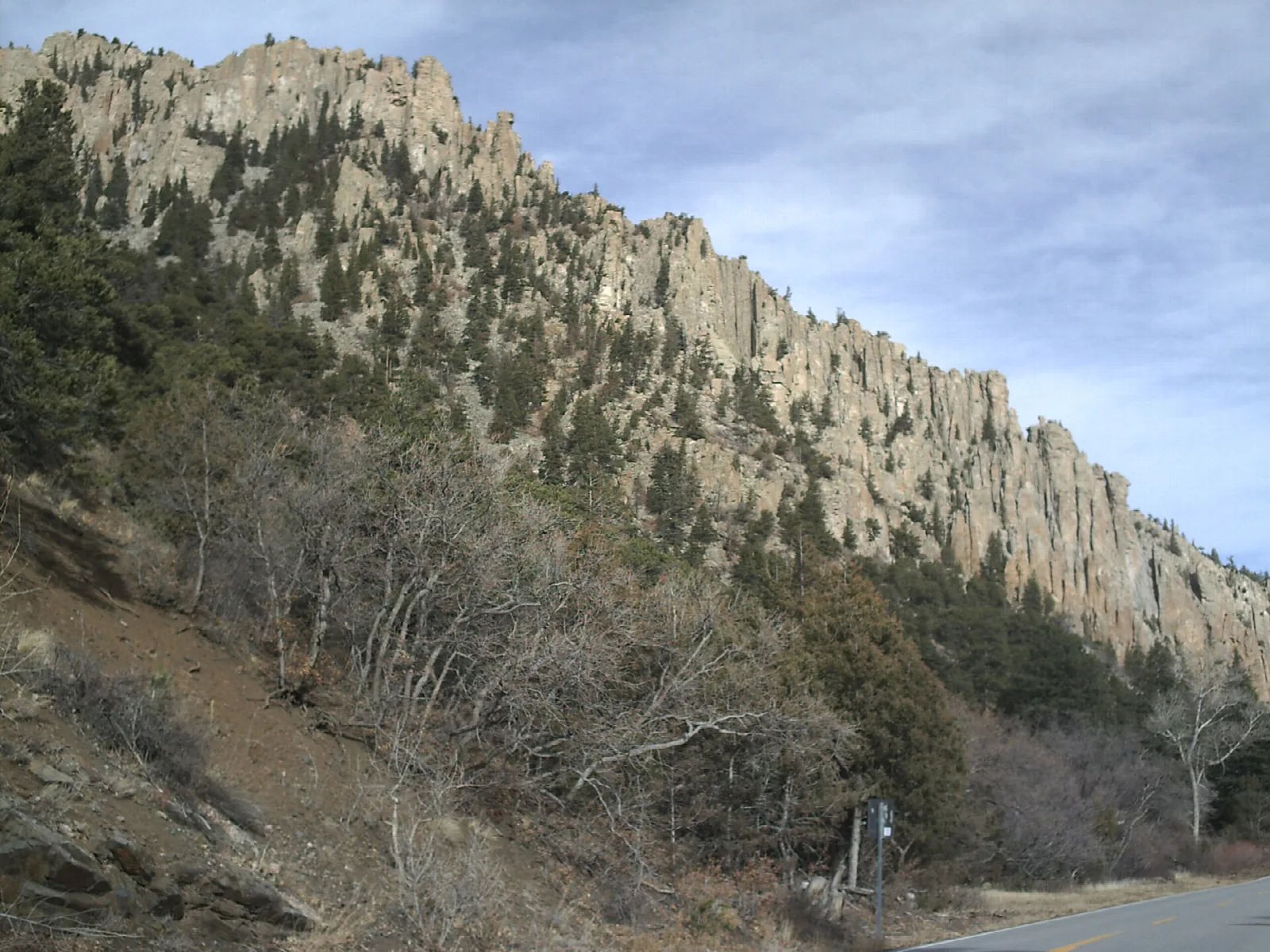 Tall pale rock cliffs rising above a road through the canyon