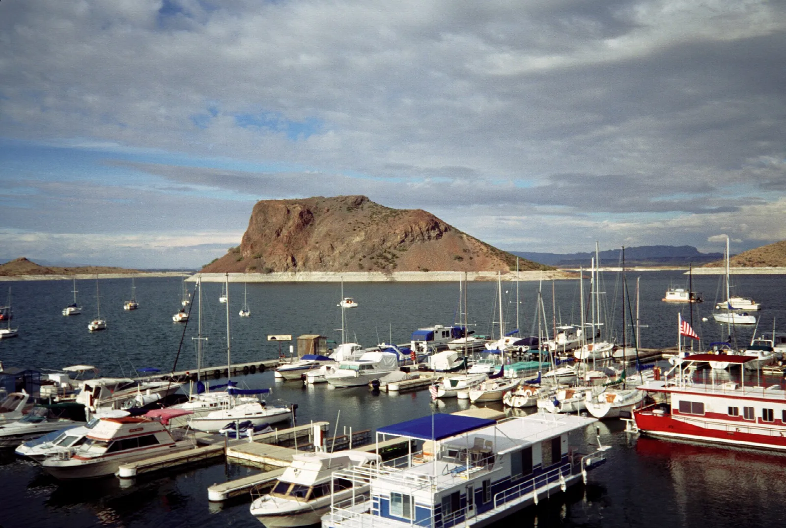 Marina full of boats below a dark rock butte