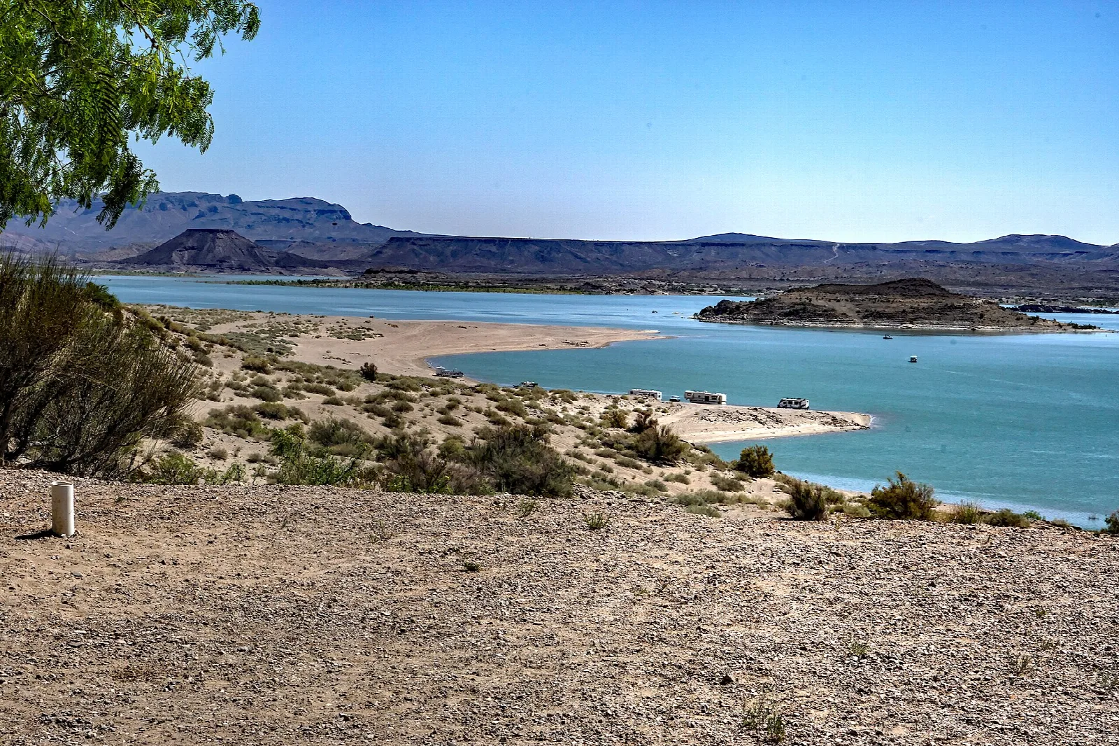 Turquoise reservoir with sandy points and desert mesas beyond