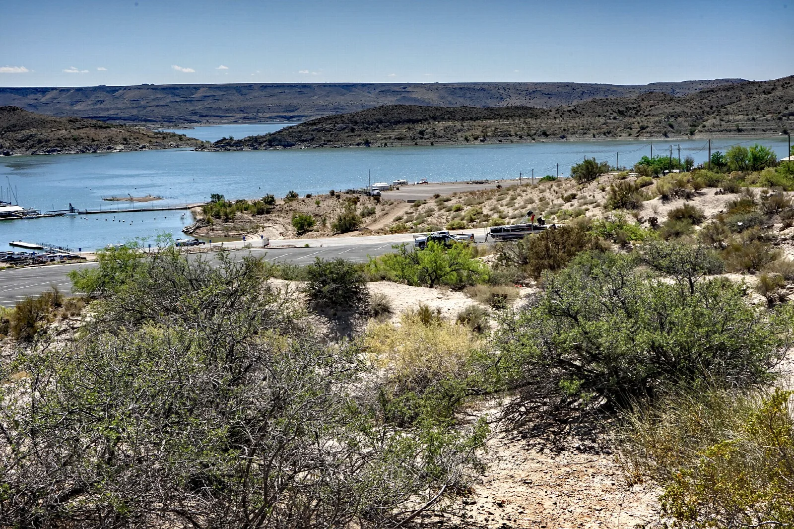 Desert shrubs and a paved road above a reservoir and boat docks