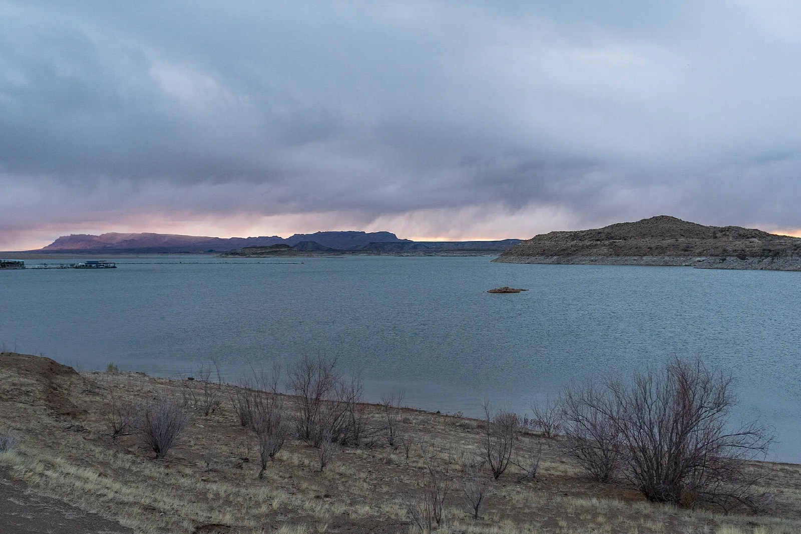 Storm clouds over a wide reservoir and desert hills at dusk