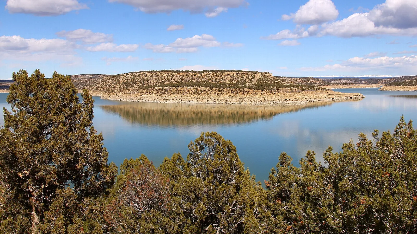 Blue lake with juniper trees and a flat-topped mesa across the water