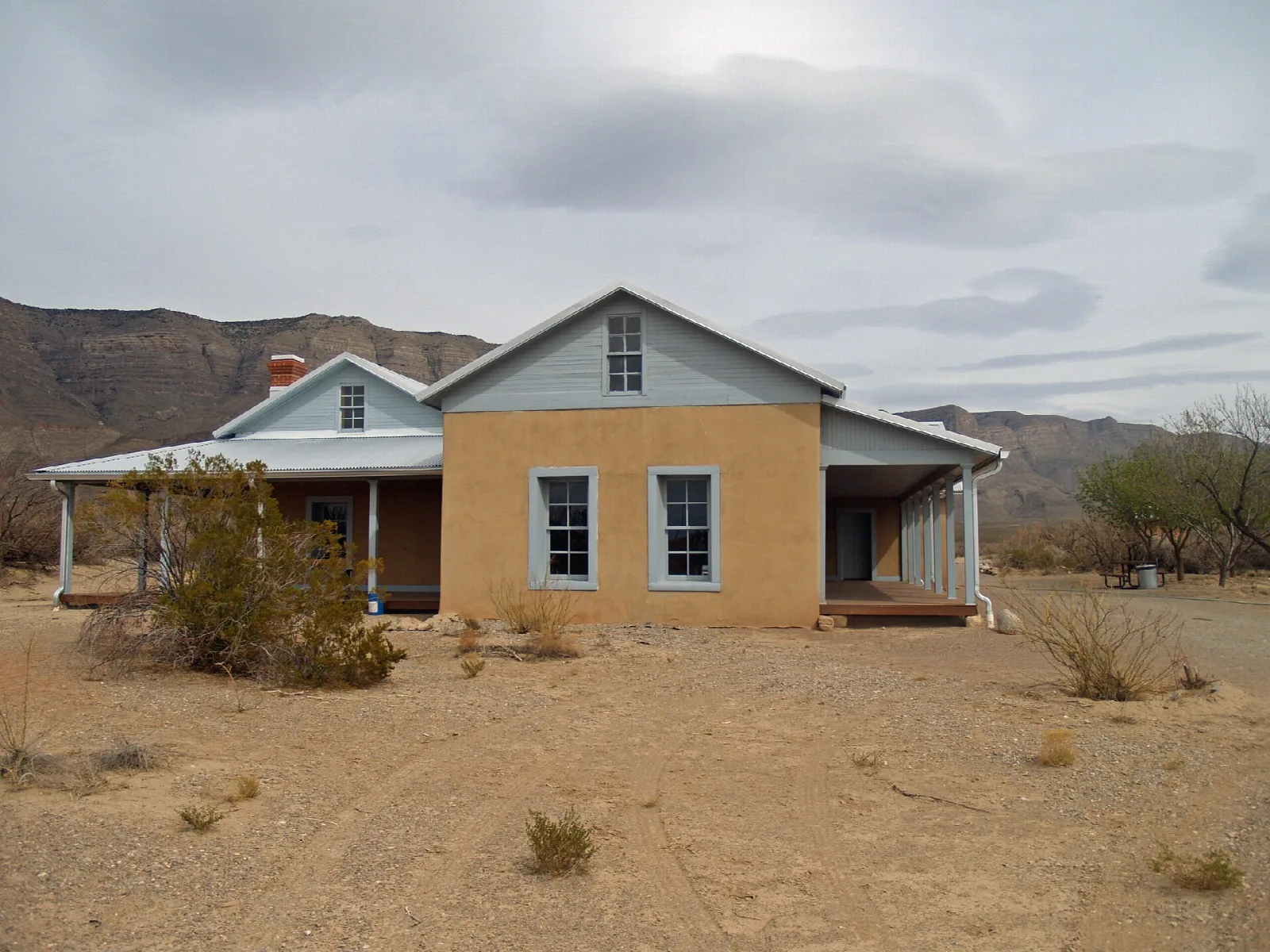 Single-story ranch house on bare desert ground with mountains behind