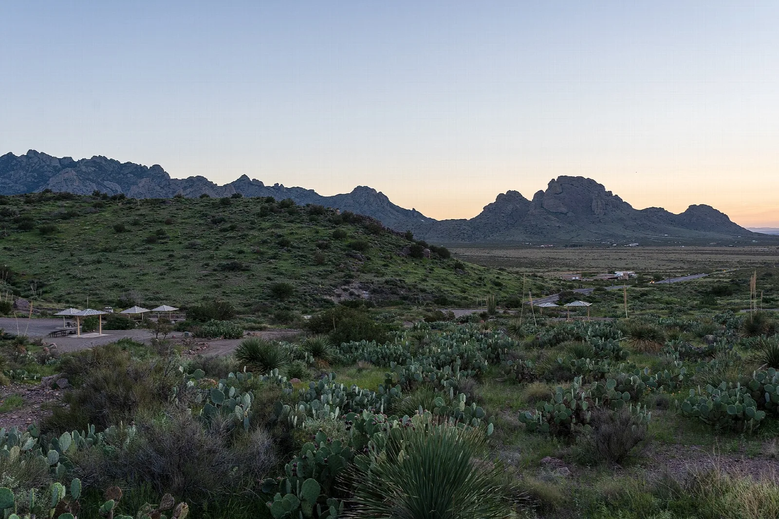 Dusk over a desert camping area with picnic shelters and jagged mountains