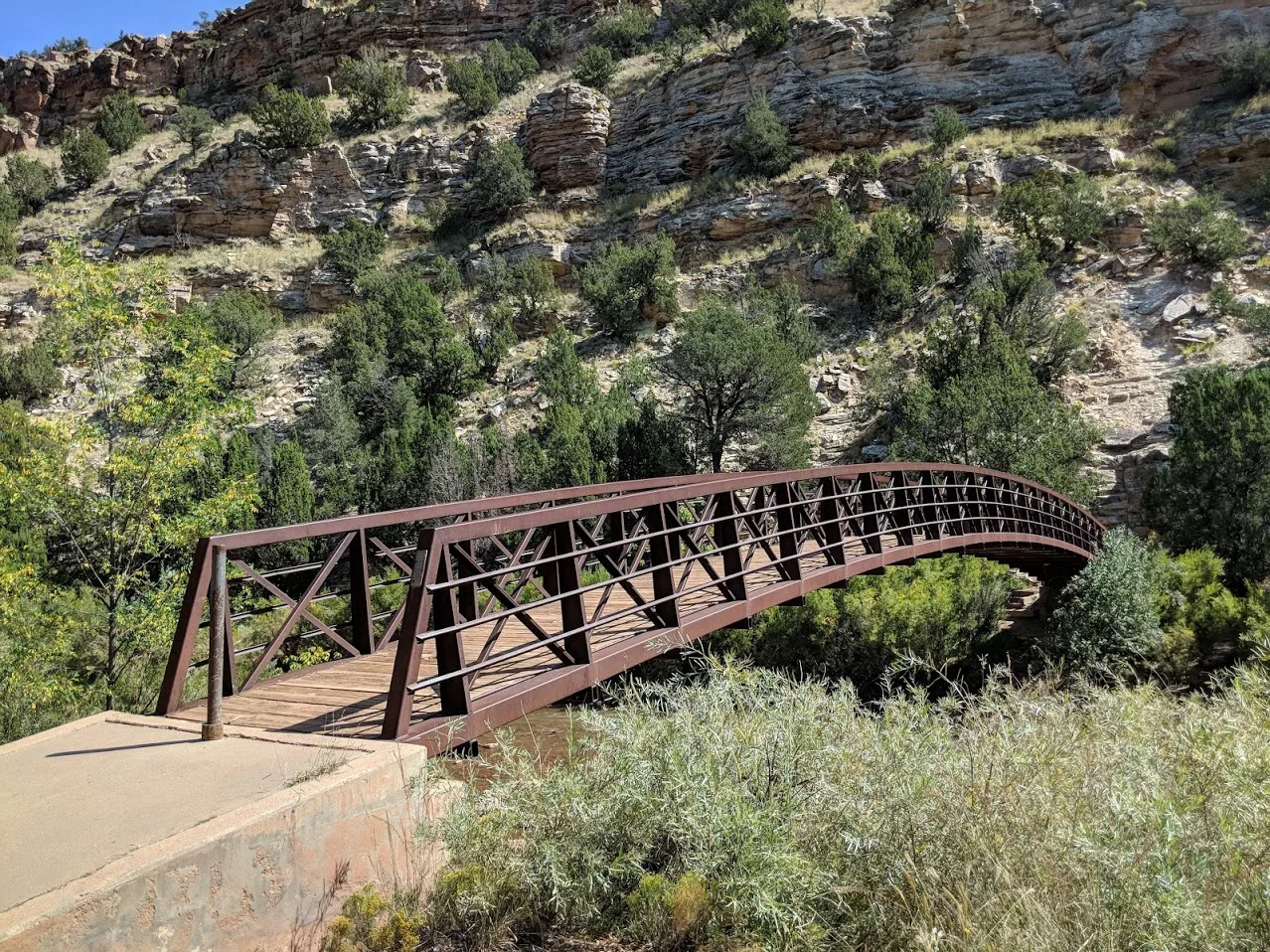 Arched metal footbridge in a canyon of pale cliffs and green trees