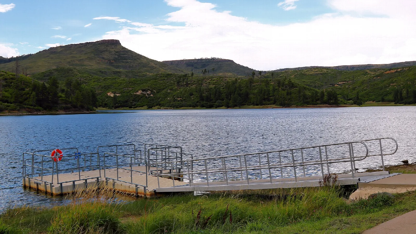 Lake with a wooden dock below a green mountain