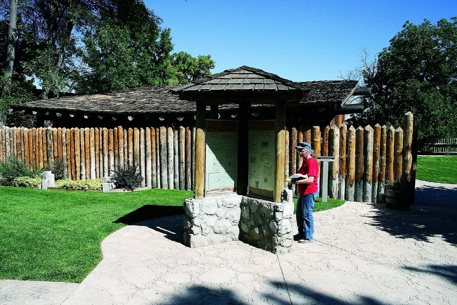 Log stockade with a roofed information kiosk and a visitor reading it
