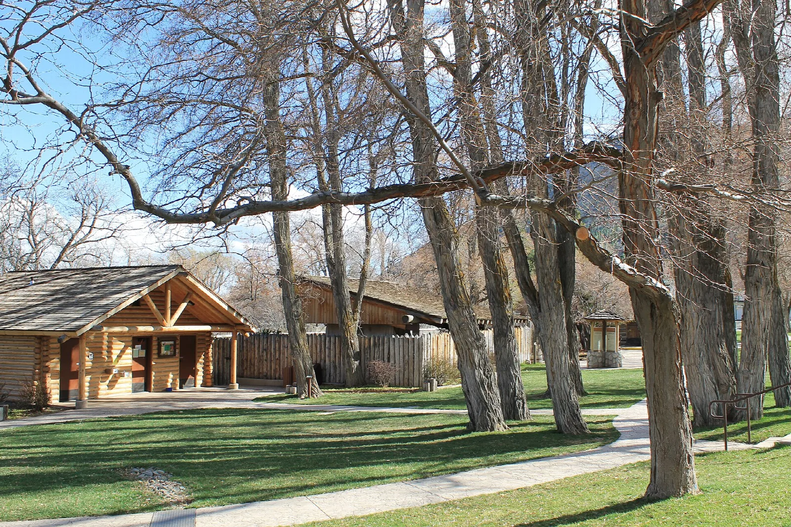 Timber-framed shelter beside a paved path and tall bare cottonwood trees