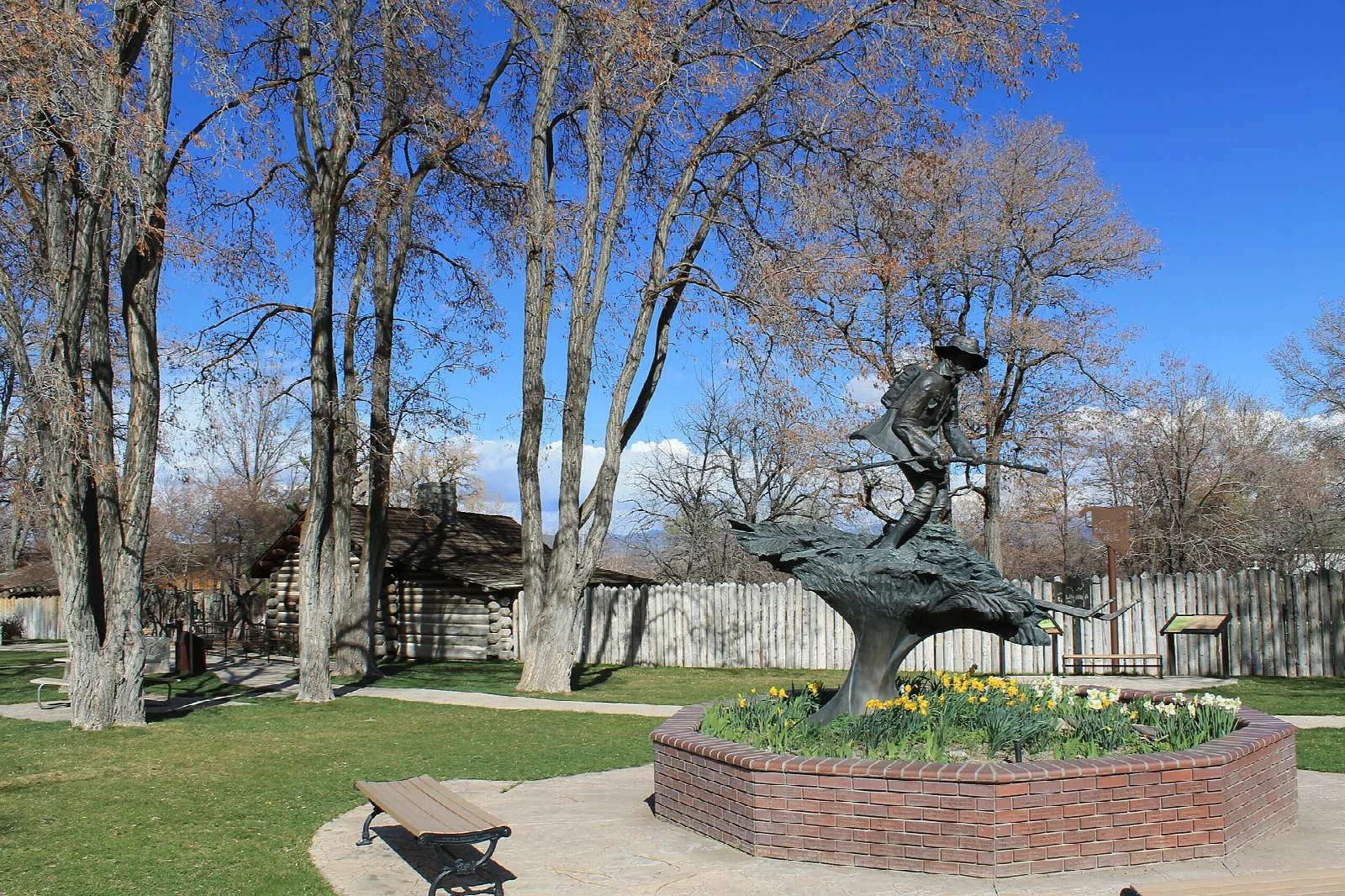 Bronze statue in a brick planter in front of a log stockade and trees