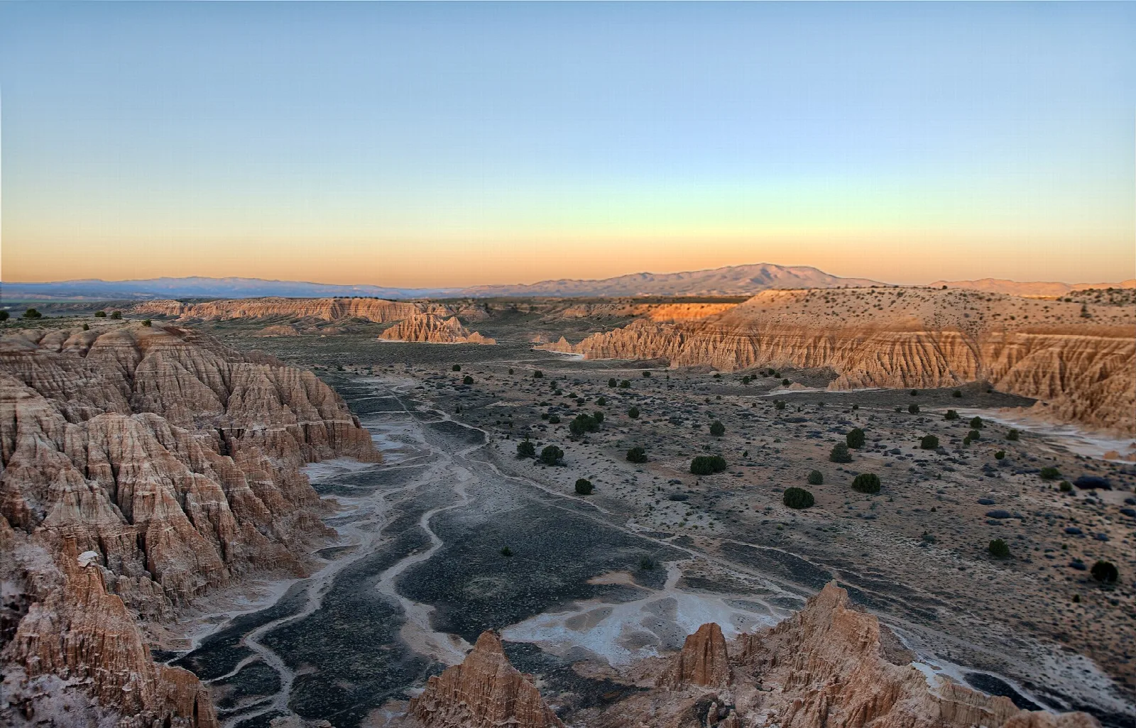Eroded clay badlands and a dry wash under an orange sunrise sky