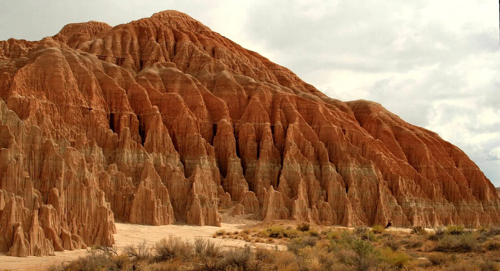 Orange eroded clay hill with ridged columns above desert scrub