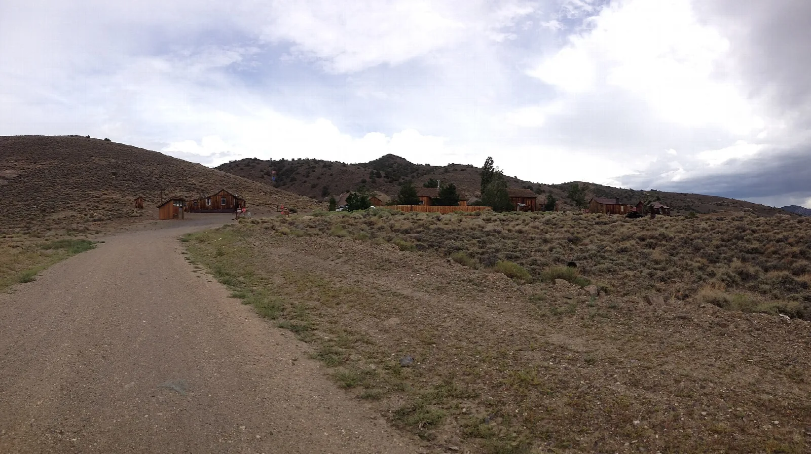 Occupied wooden buildings beside a gravel road with sagebrush hills behind