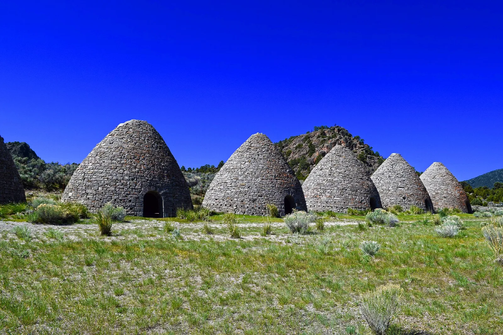 Five stone beehive ovens on green grass under a deep blue sky