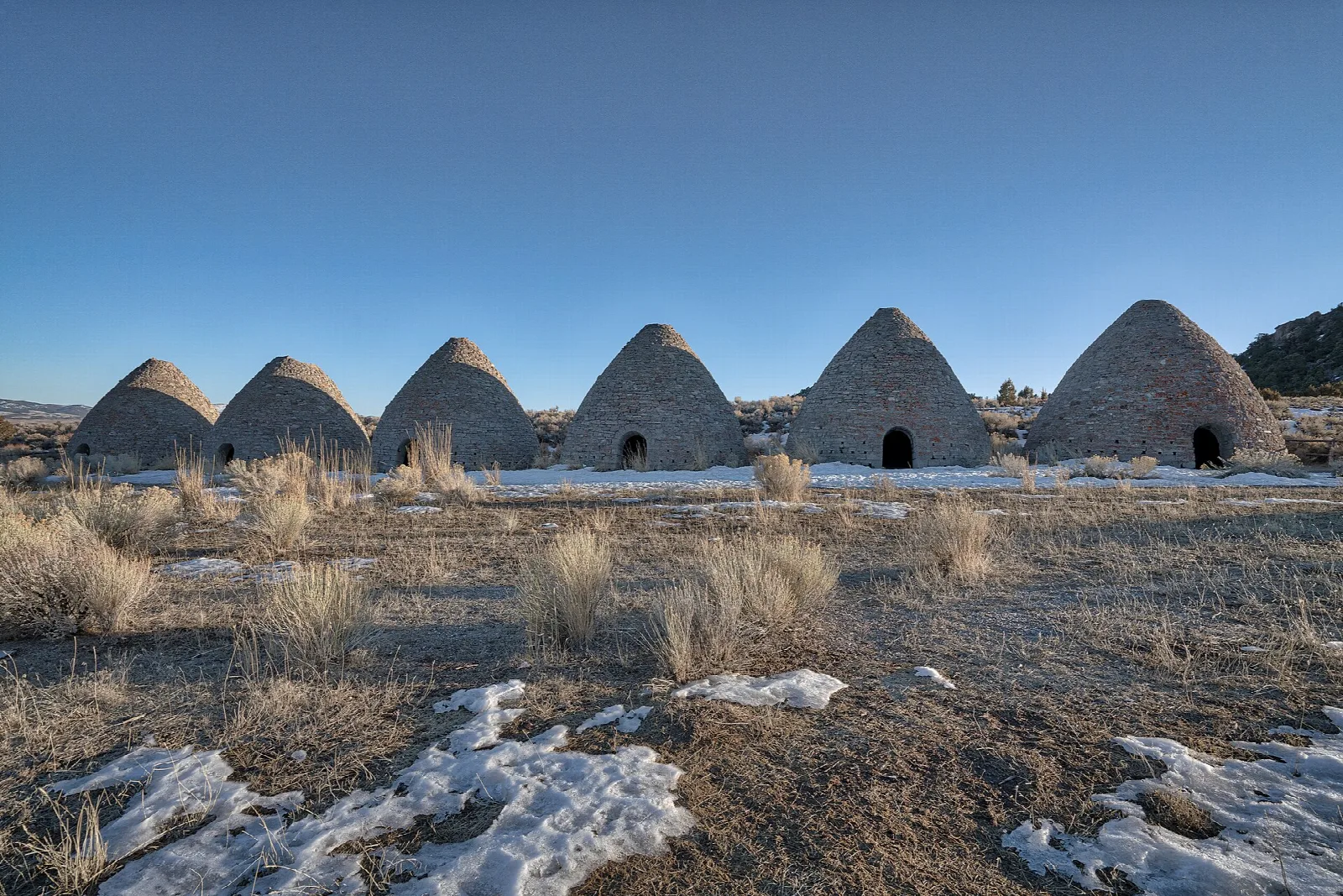 Row of stone ovens in dry grass with patches of snow