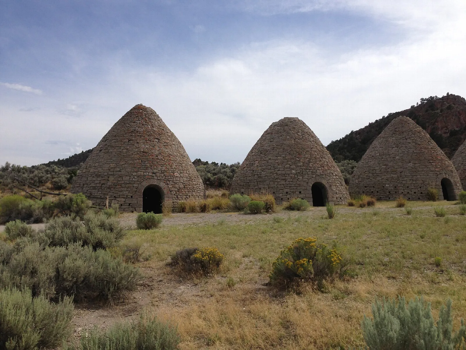 Three stone ovens in sagebrush with a dark hill behind