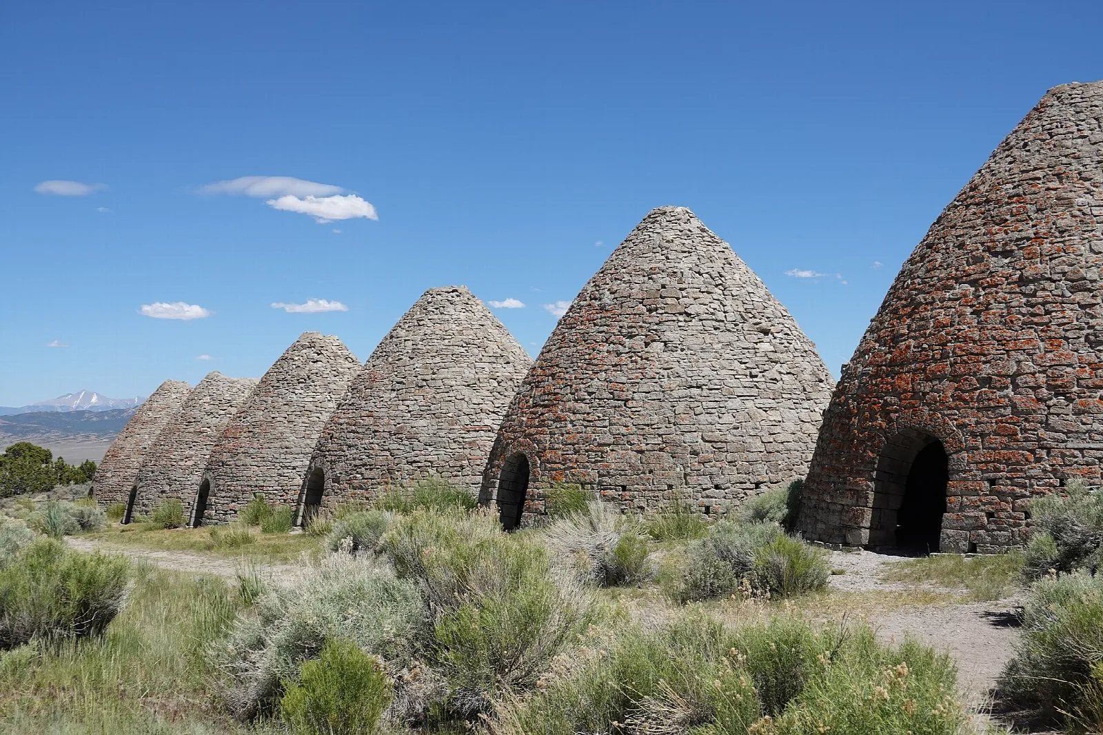 Row of beehive-shaped stone ovens among sagebrush with mountains behind